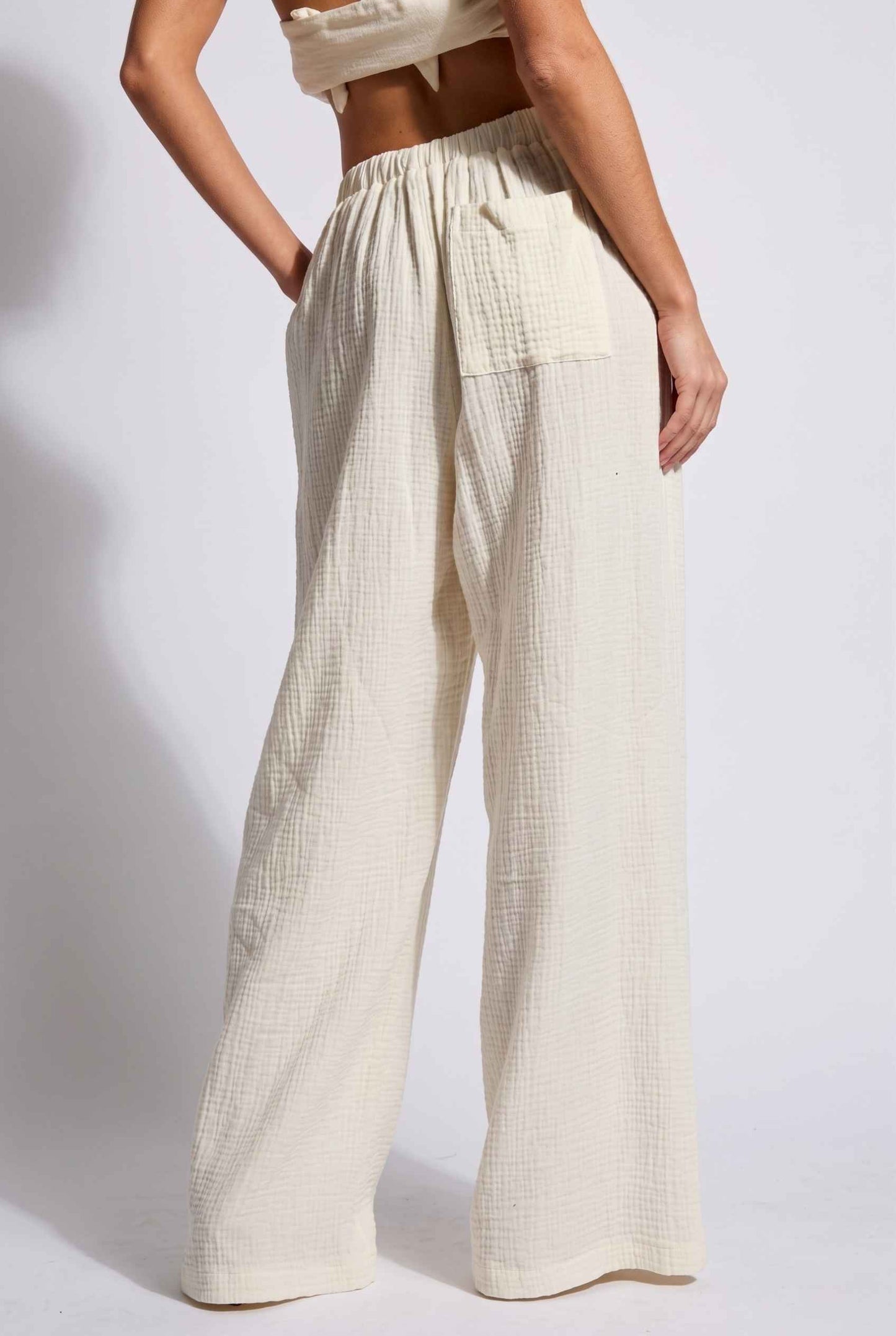 Model wearing Celine High-Waisted Gauze Pant 100% Cotton Wide-Leg Resort Pant in Off White paired with matching halter crop top close back view