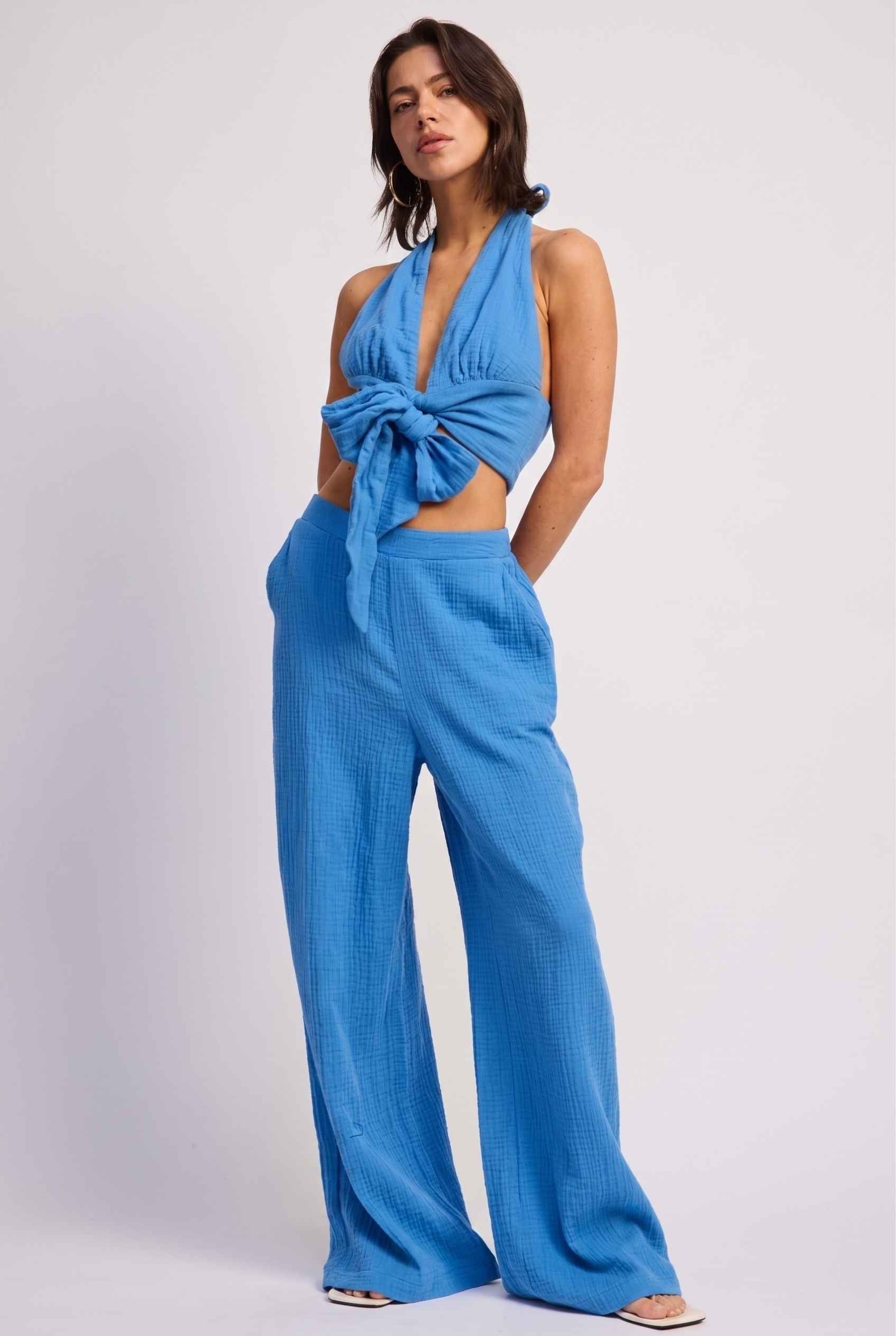 Model wearing Celine High-Waisted Gauze Pant 100% Cotton Wide-Leg Resort Pant in Blue paired with matching halter crop top and sandals