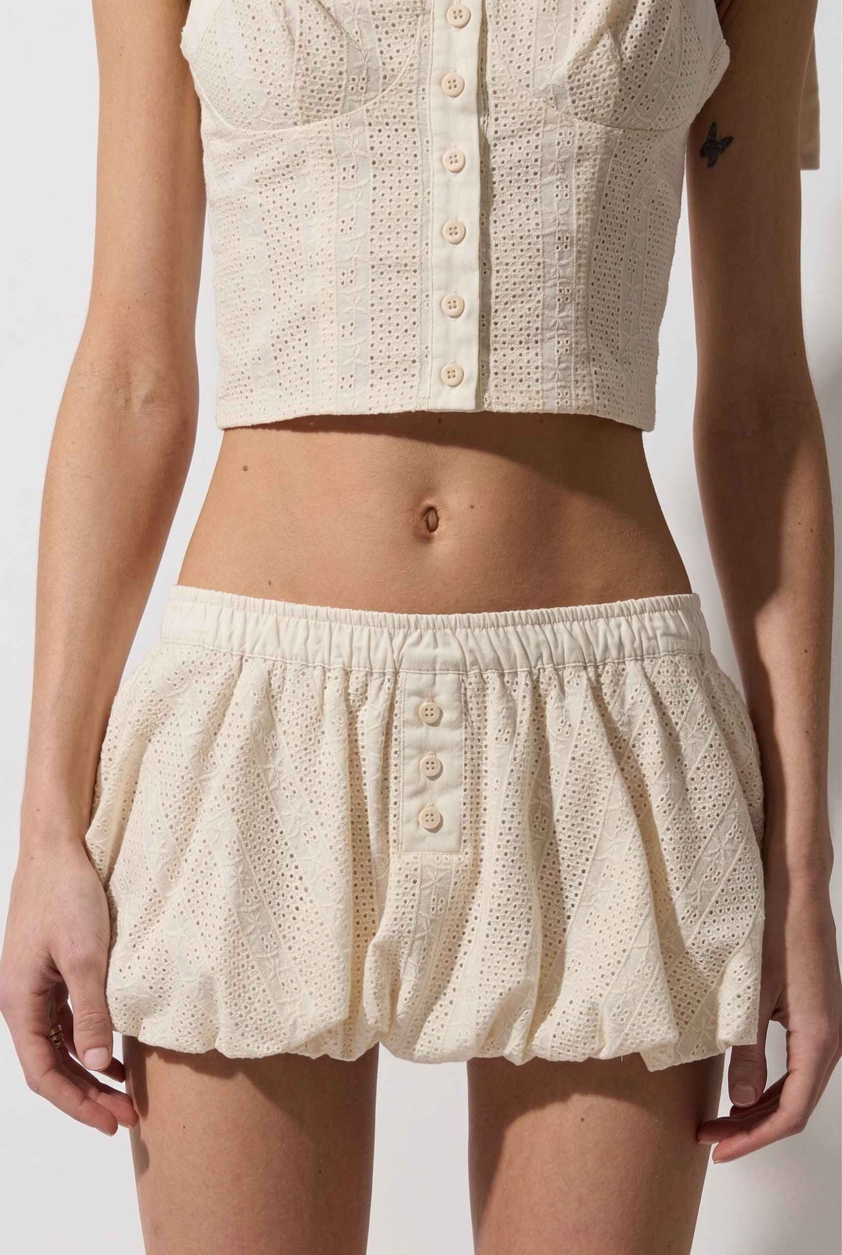 Woman wearing a cream-colored textured top and Chloe Skirt Cream Cotton Eyelet Bubble Hem Mini Skirt on a plain background