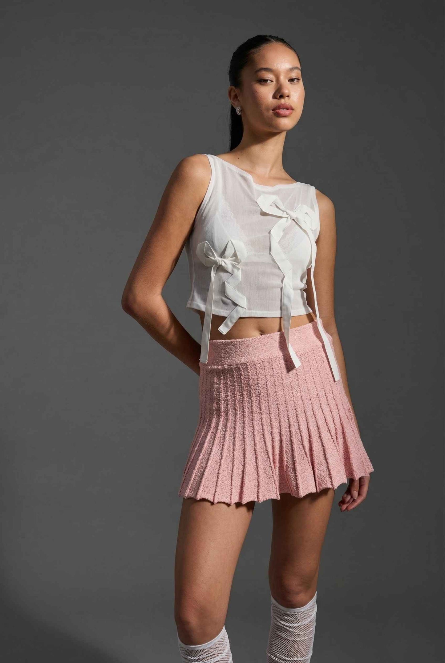 Woman wearing a top and Chloe Skirt Textured Knit Pleated Mini Skirt in Pink against a gray background