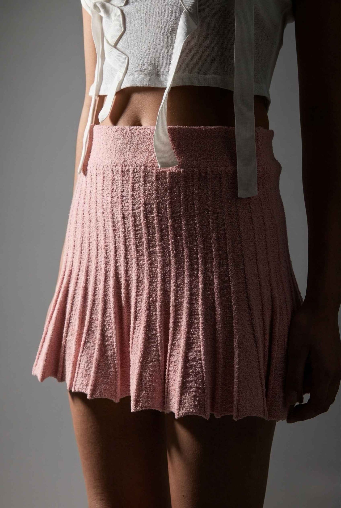 Woman wearing a Chloe Skirt Textured Knit Pleated Mini Skirt in Pink and light-colored top against a gray background