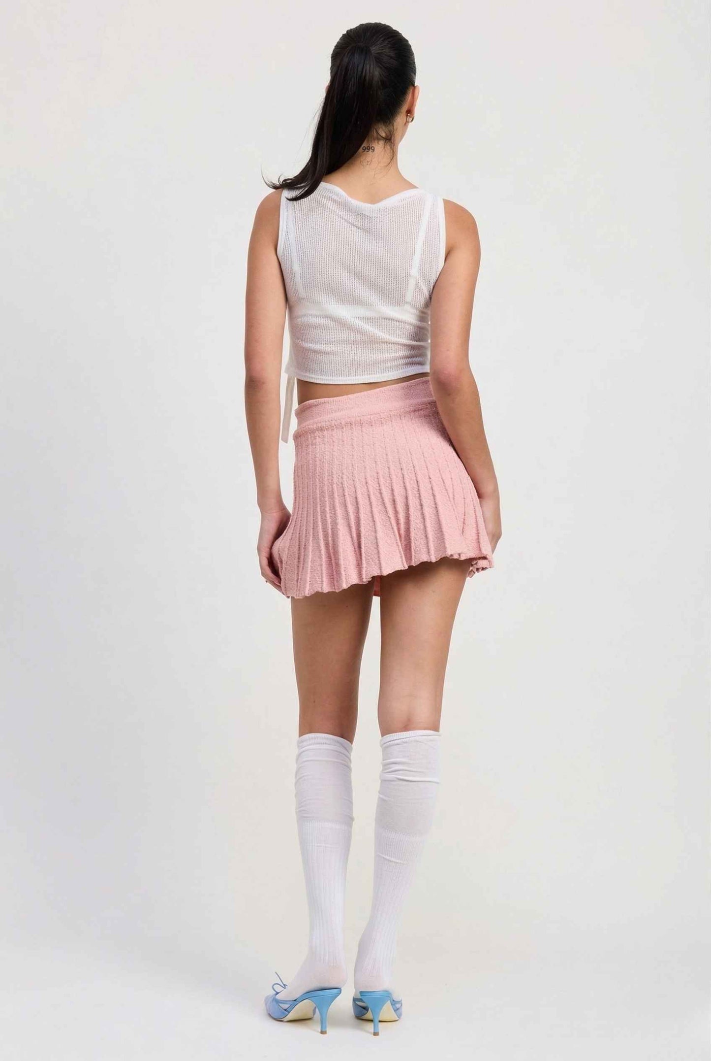 Woman wearing a sleeveless top and Chloe Skirt Textured Knit Pleated Mini Skirt in Pink on a plain background