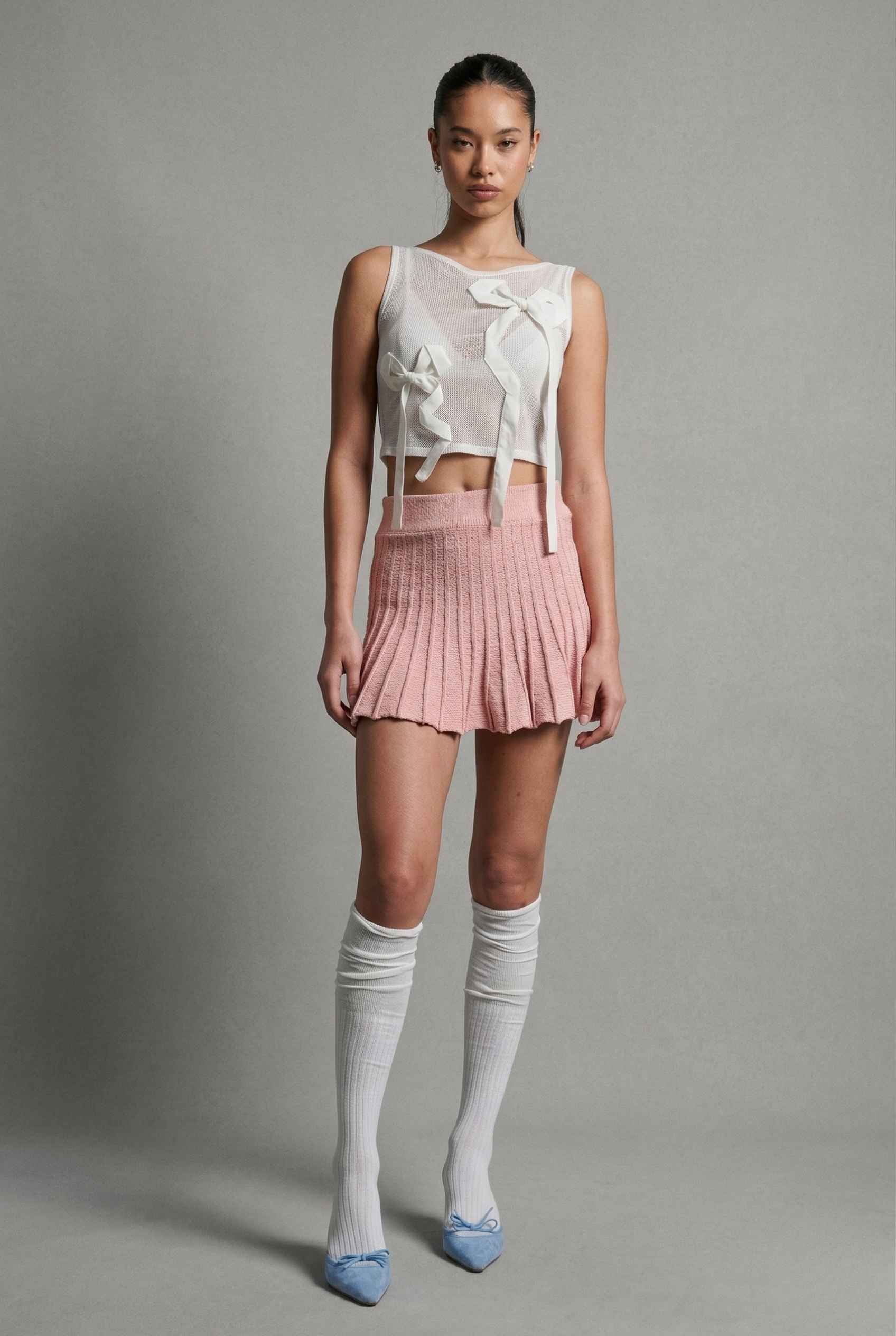 Woman wearing a sleeveless top with a bow and a Chloe Skirt Textured Knit Pleated Mini Skirt in Pink on a gray background