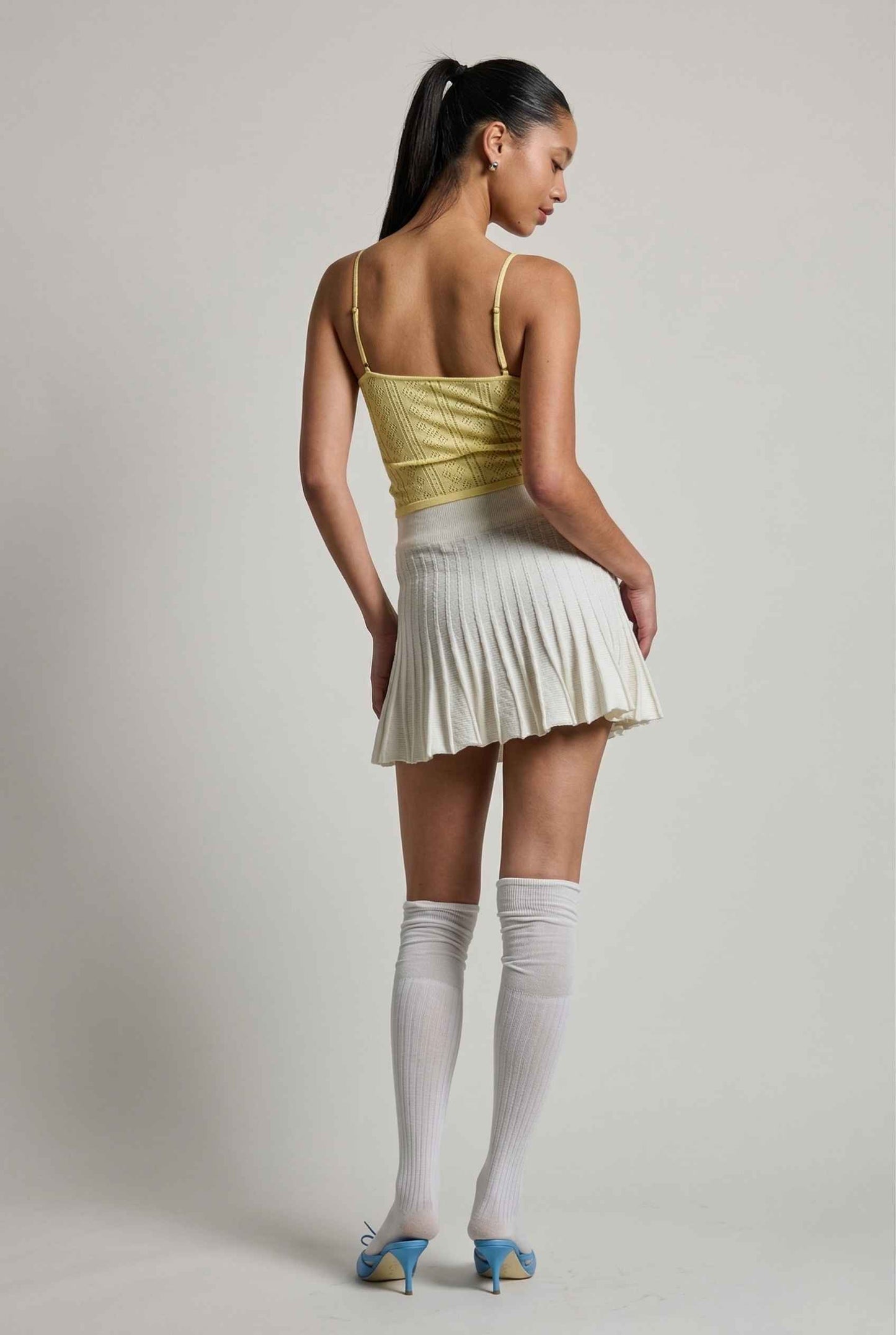 Woman wearing a yellow top and Chloe Skirt Textured Knit Pleated Mini Skirt in White with knee-high socks on a plain background
