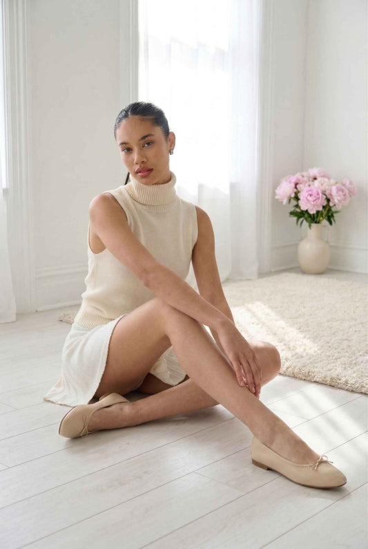 Woman sitting on a white floor wearing a beige sleeveless top and Chloe Skirt Textured Knit Pleated Mini Skirt in White with matching shoes, in a bright room.