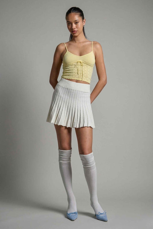 Woman wearing a yellow top, Chloe Skirt Textured Knit Pleated Mini Skirt in White, and knee-high socks against a gray background