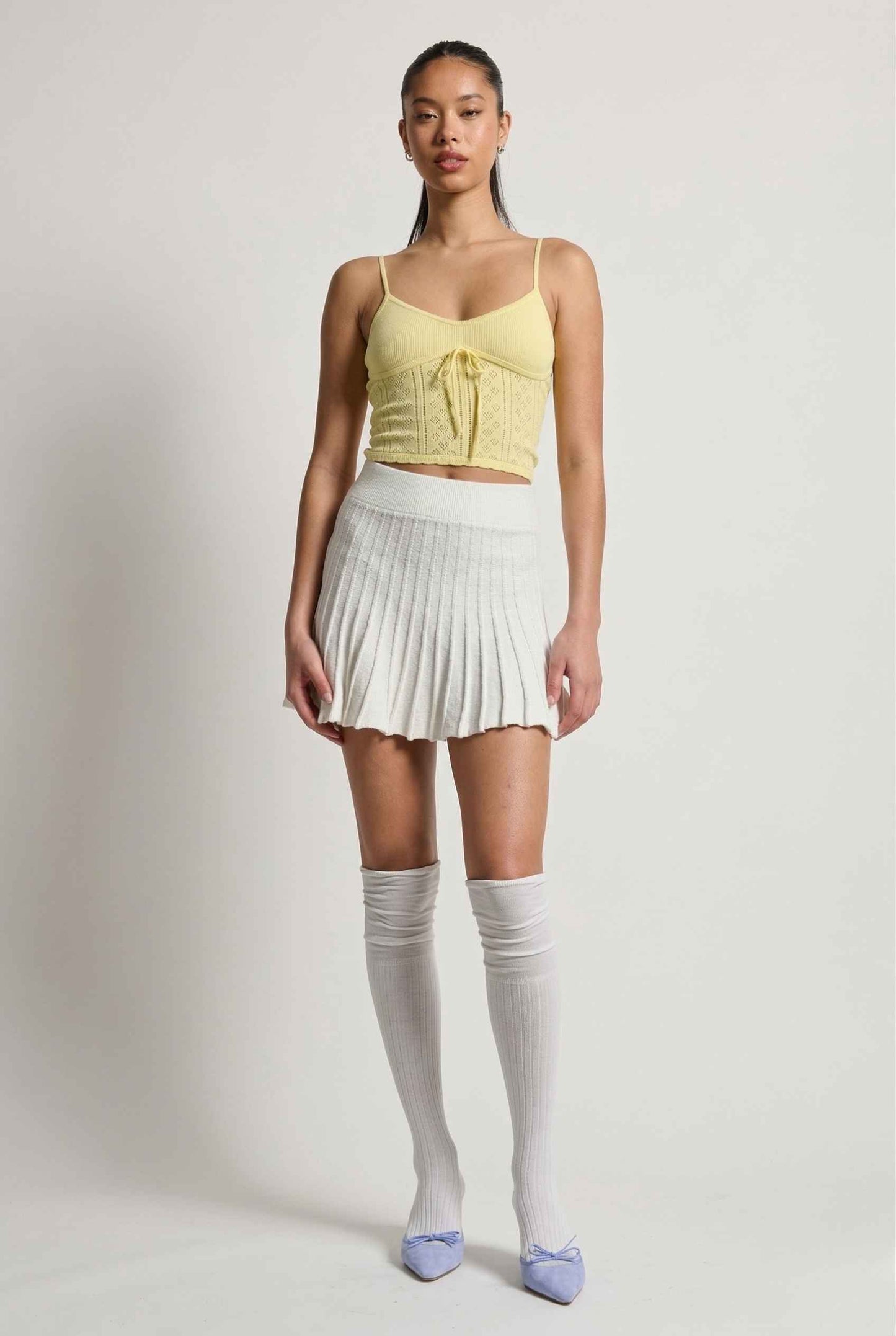 Woman wearing a yellow top, Chloe Skirt Textured Knit Pleated Mini Skirt in White, and knee-high socks on a plain background