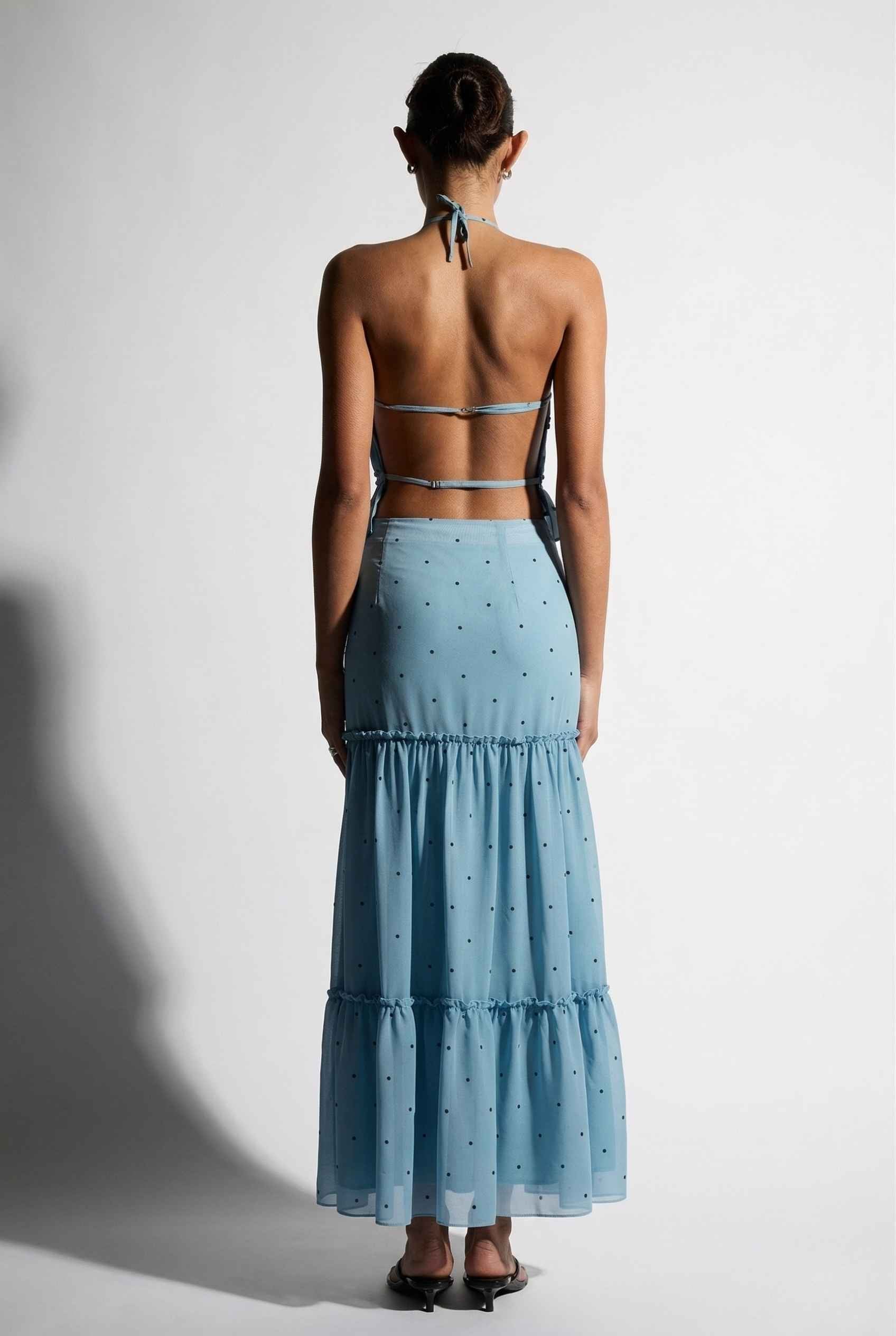 Woman wearing a Clara Skirt Blue Tiered Ruffle Polka Dot Midi Skirt with a plain background