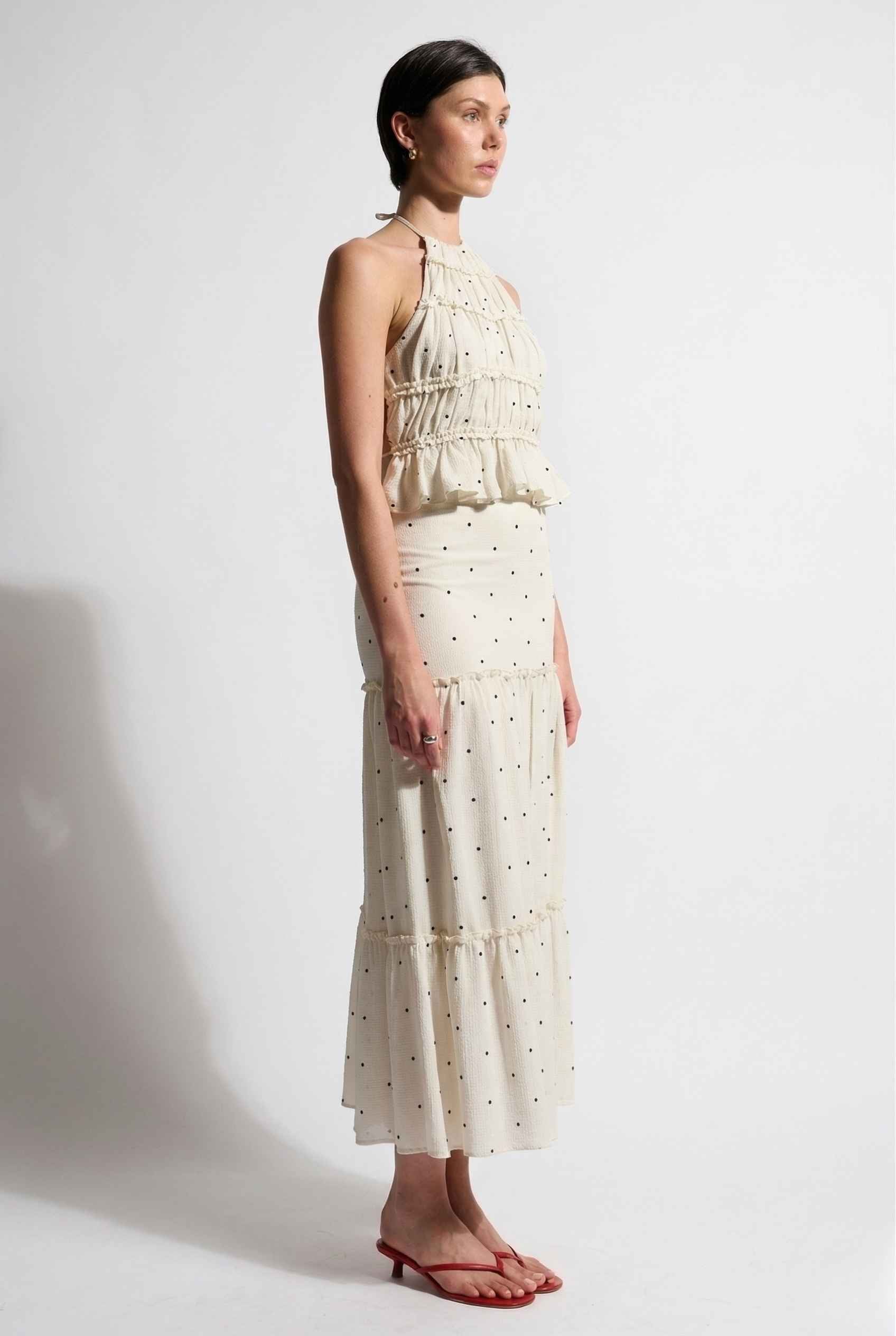Woman wearing a Clara Skirt White Tiered Ruffle Polka Dot Midi Skirt with gold polka dots on a white background