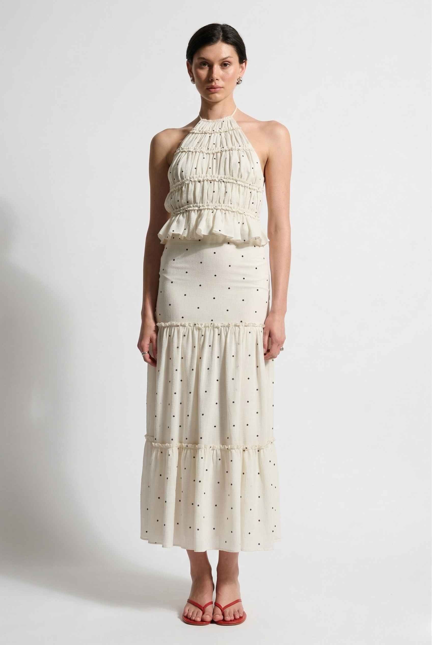 Woman wearing a Clara Skirt White Tiered Ruffle Polka Dot Midi Skirt with a polka dot pattern on a plain background