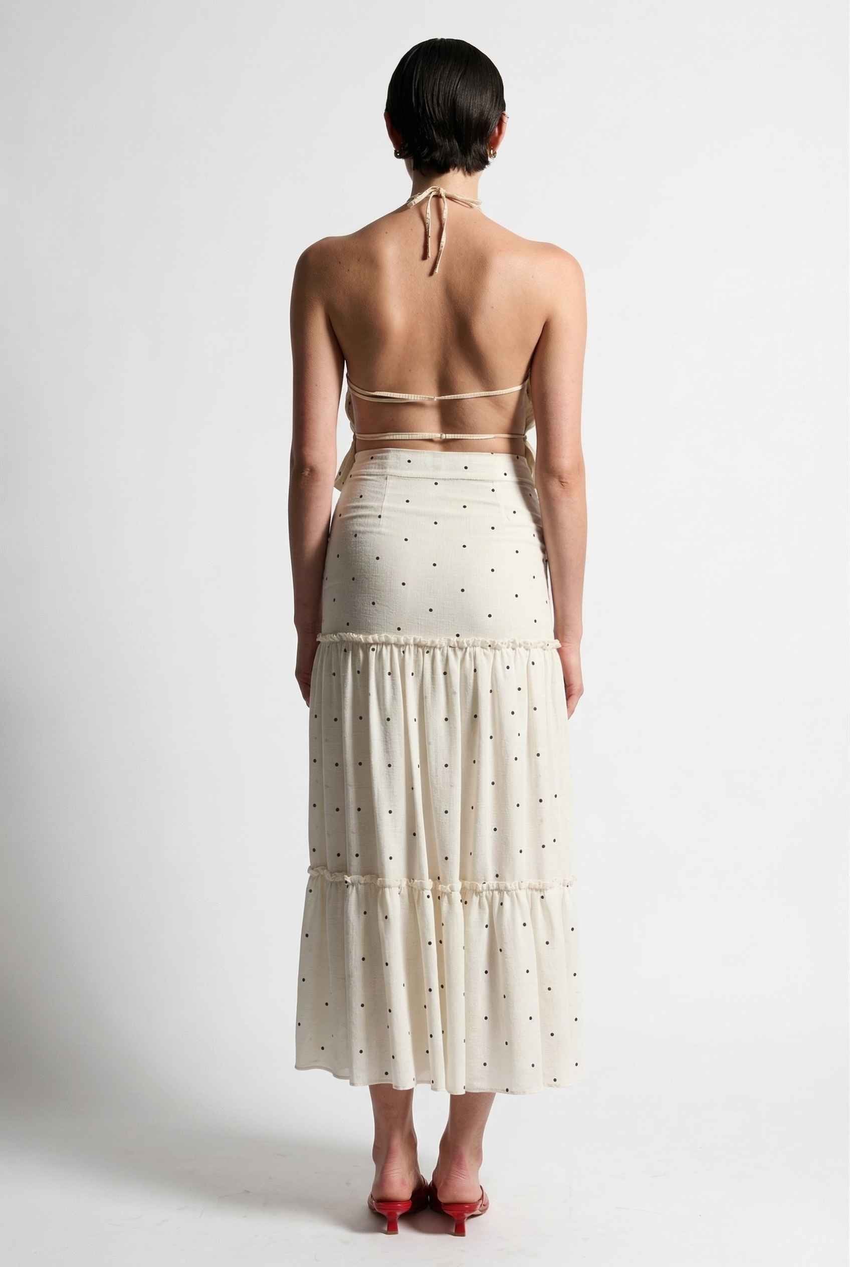 Woman wearing a Clara Skirt White Tiered Ruffle Polka Dot Midi Skirt with a halter top on a plain background