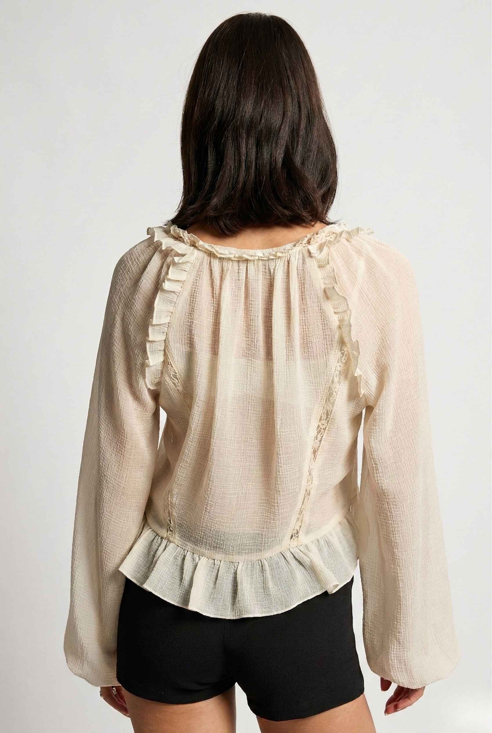 Woman wearing a Clara Top Cream Sheer Chiffon Tie-Front Balloon Sleeve Blouse with ruffled details on a white background