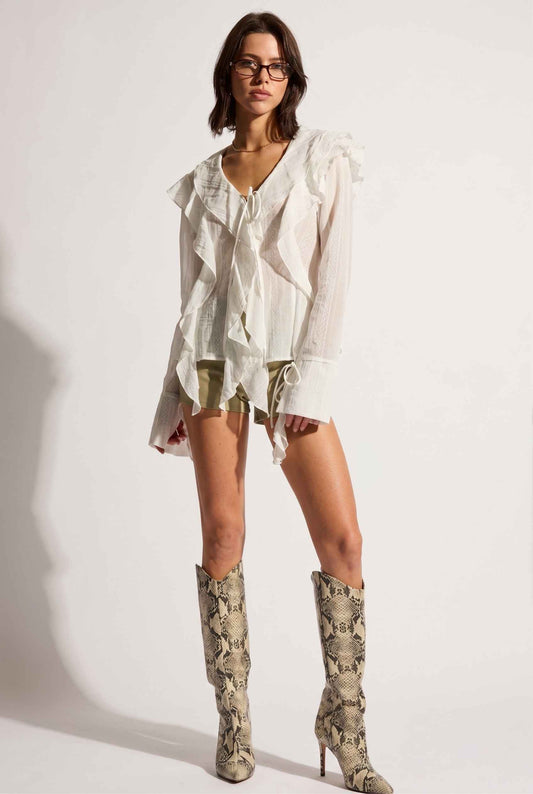 Model wearing Clarisse Crinkled Chiffon Blouse Ruffled V-Neck Tie in White with shorts and tall heeled snake boots