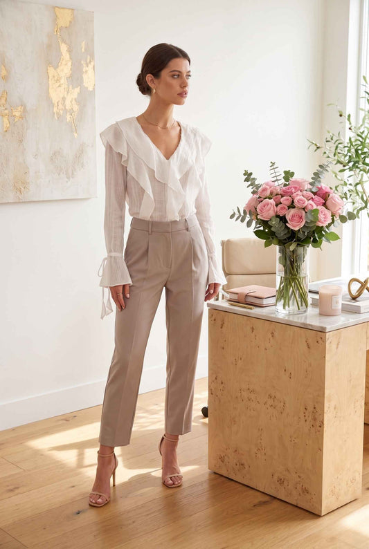 Model wearing Clarisse Crinkled Chiffon Blouse Ruffled V-Neck Tie in White with pleated trousers and heels posing in feminine office