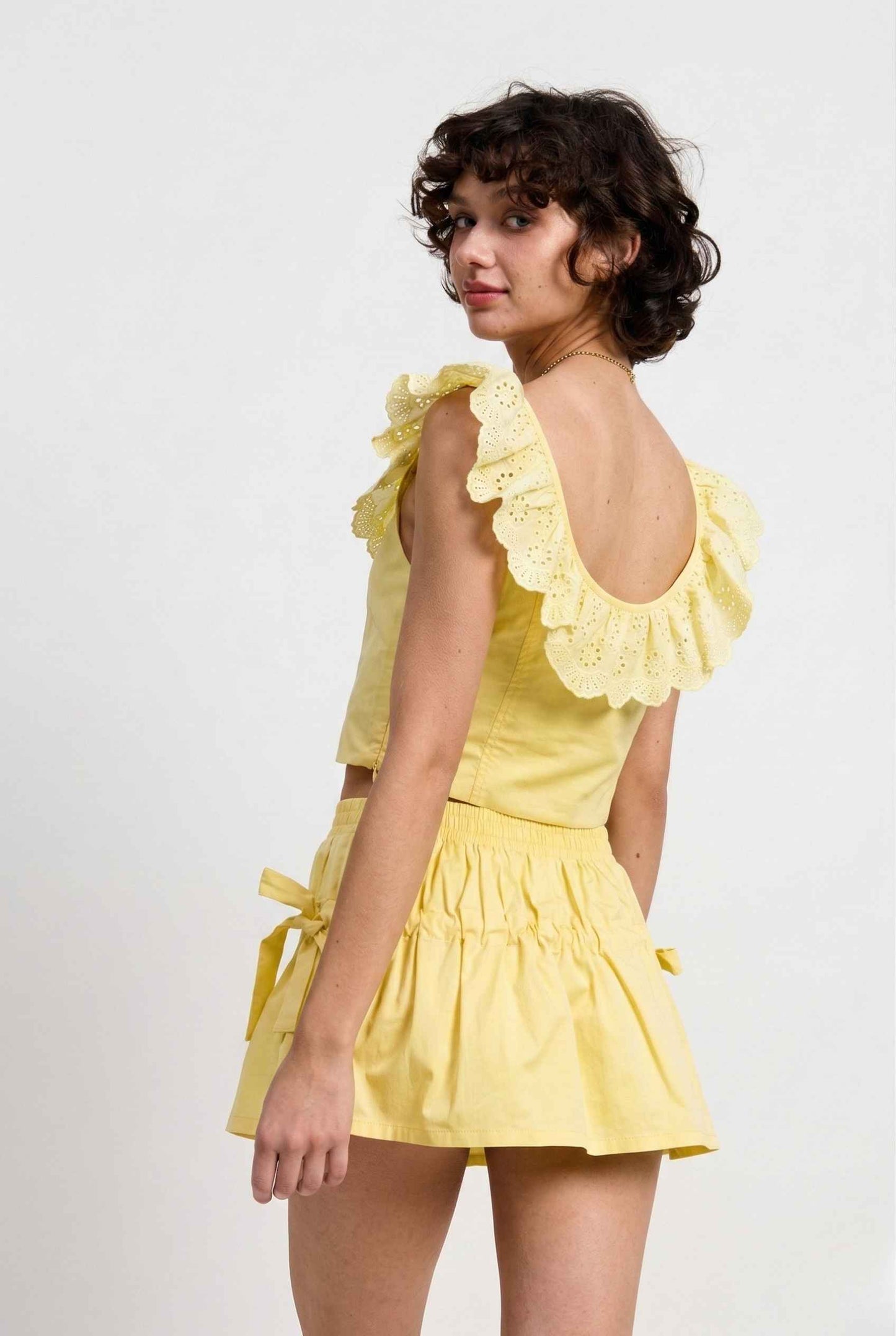Woman wearing a Clementine Top Lemon Yellow Cotton Eyelet Ruffle Corset with ruffled sleeves on a white background
