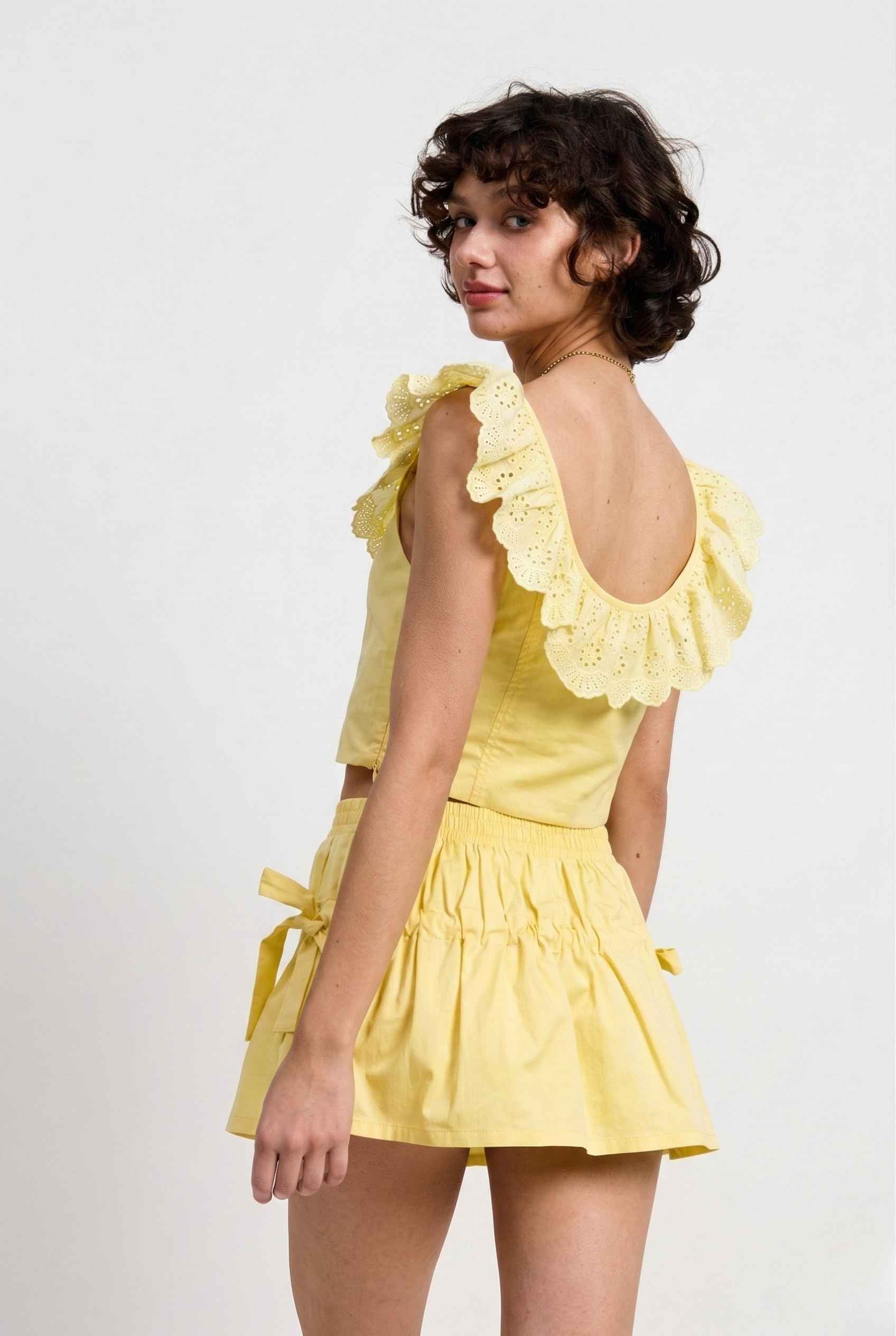 Woman wearing a Clementine Top Lemon Yellow Cotton Eyelet Ruffle Corset with ruffled sleeves on a white background