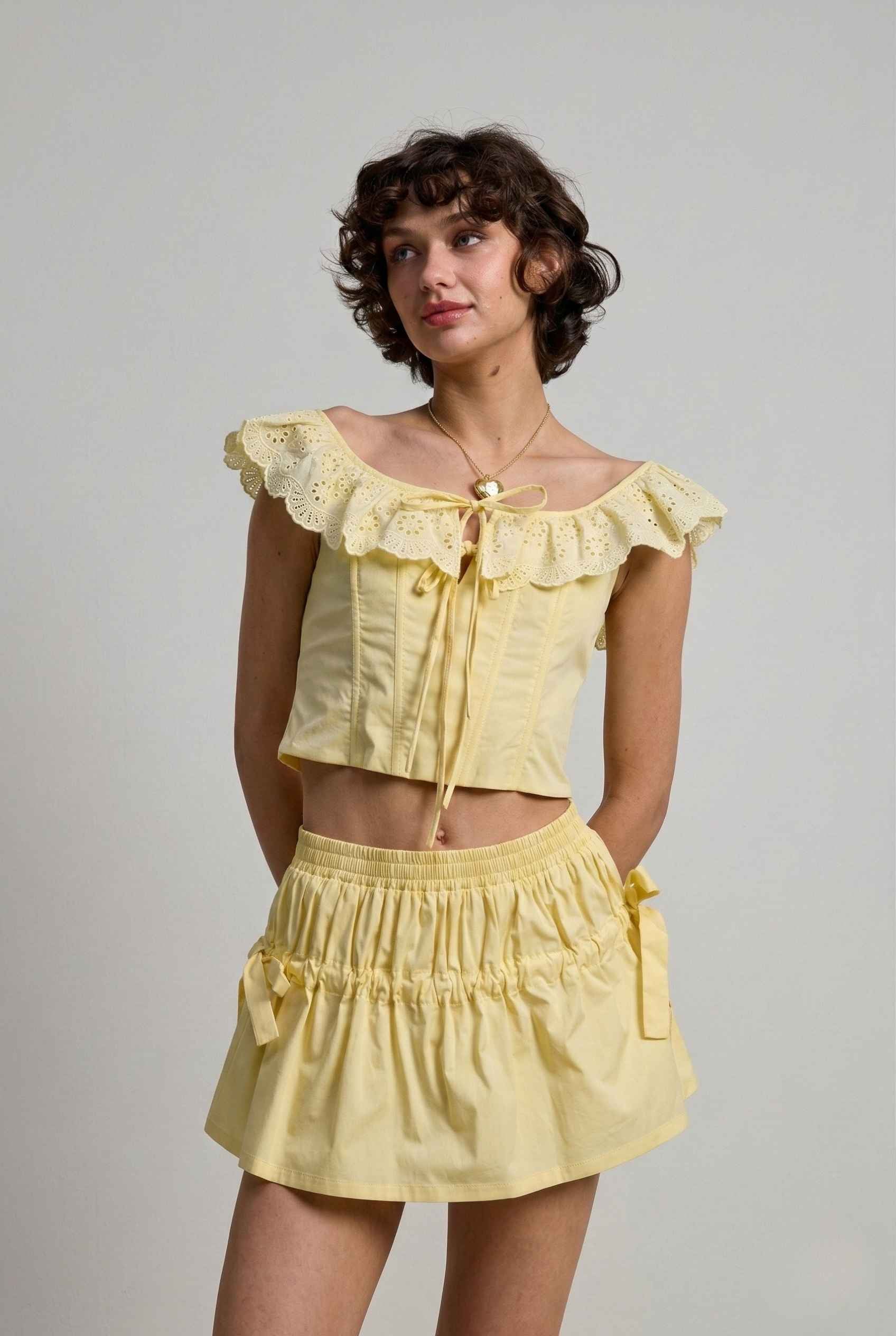 Woman wearing a Clementine Top Lemon Yellow Cotton Eyelet Ruffle Corset with ruffled details on a plain background