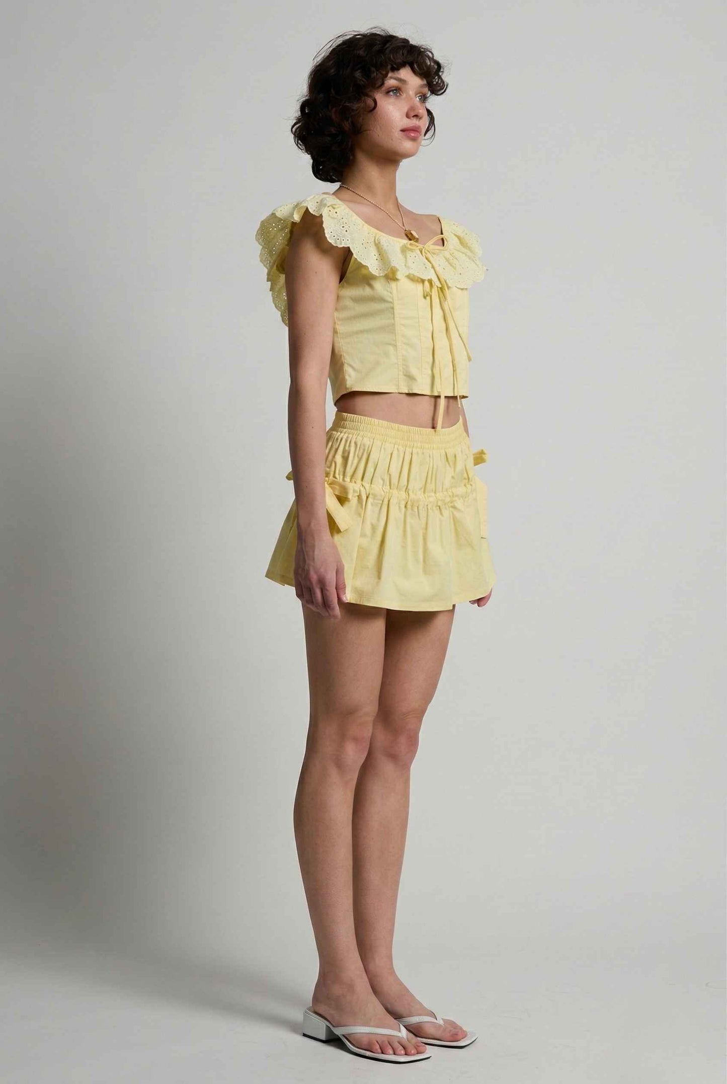 Woman wearing a Clementine Top Lemon Yellow Cotton Eyelet Ruffle Corset with ruffled sleeves against a plain background