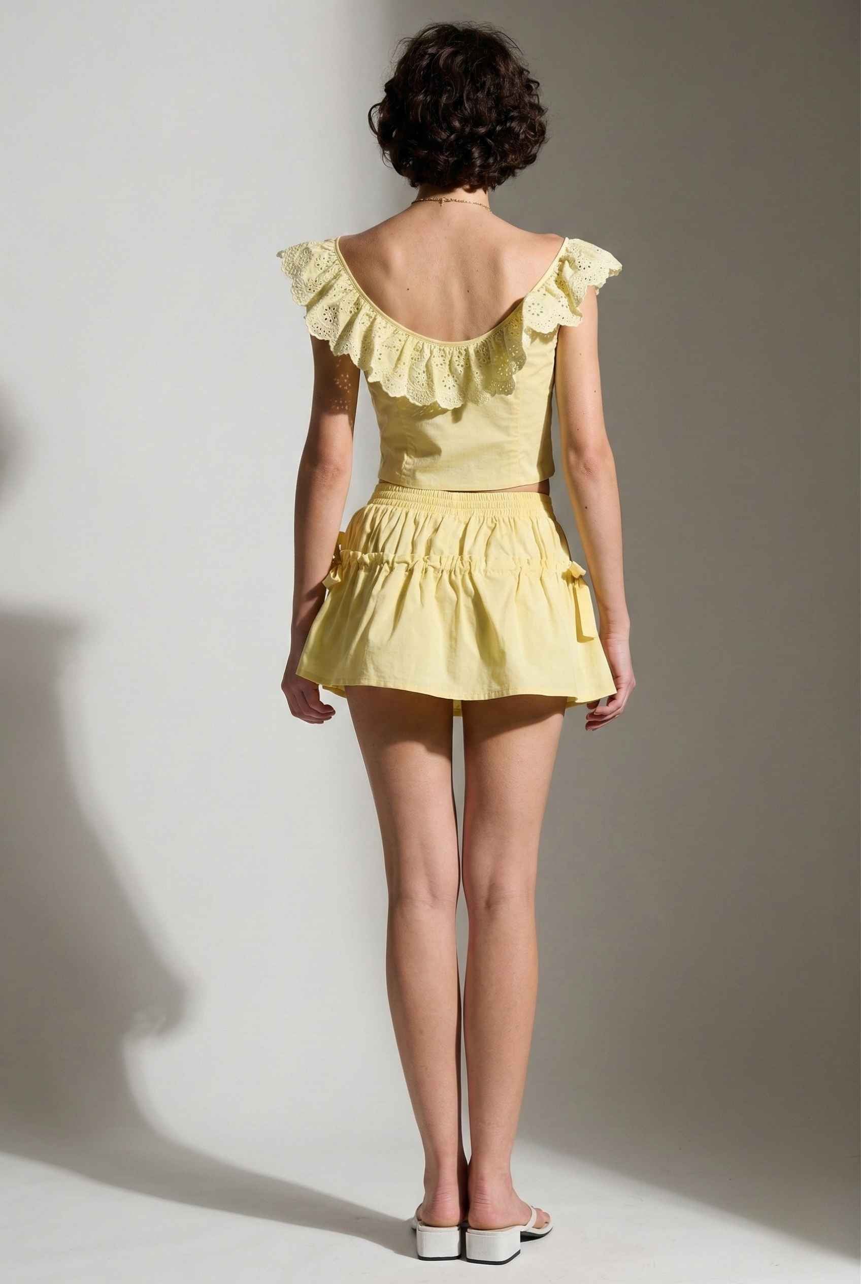 Woman wearing a Clementine Top Lemon Yellow Cotton Eyelet Ruffle Corset and skirt against a plain background