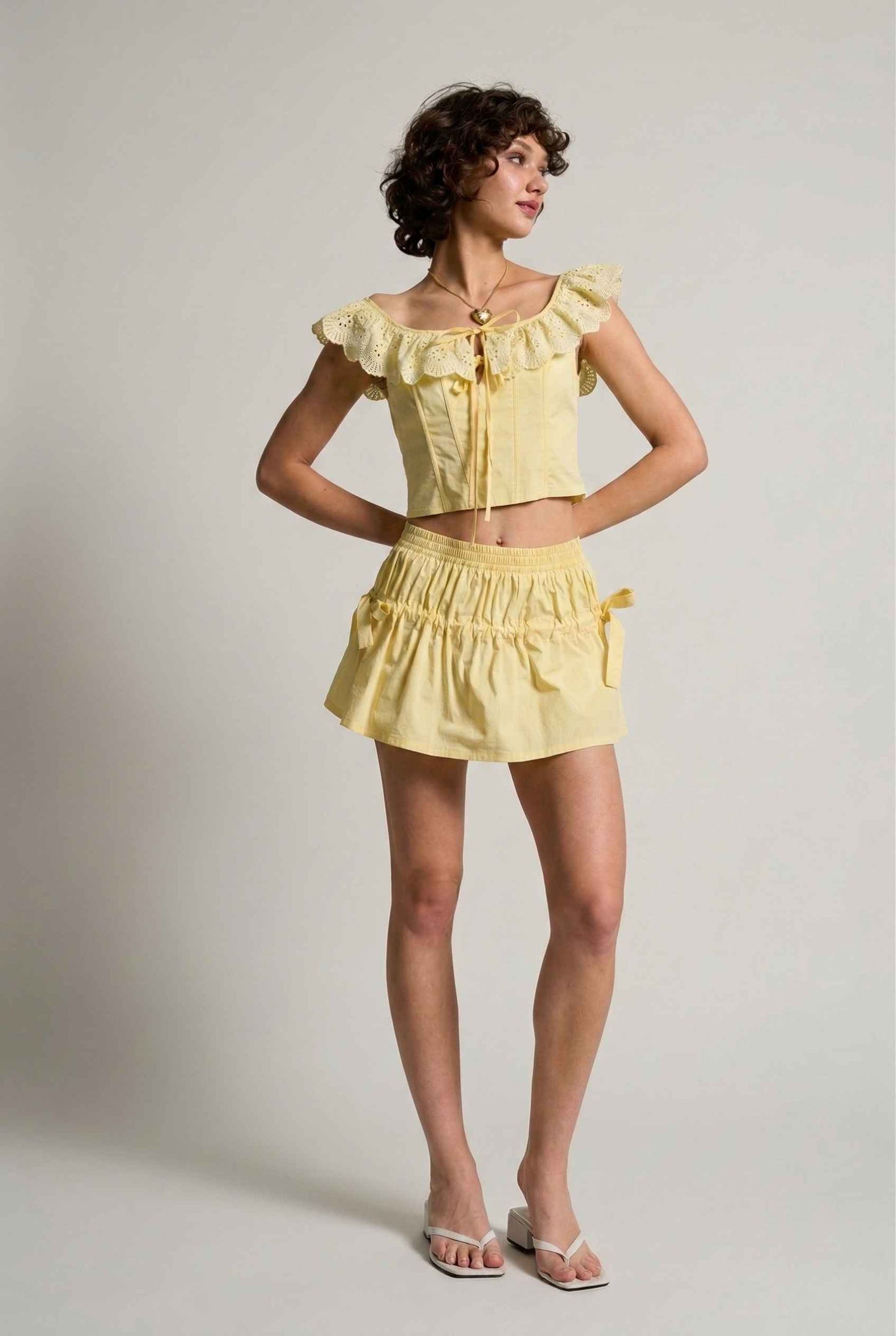 Woman wearing a Clementine Top Lemon Yellow Cotton Eyelet Ruffle Corset plain background