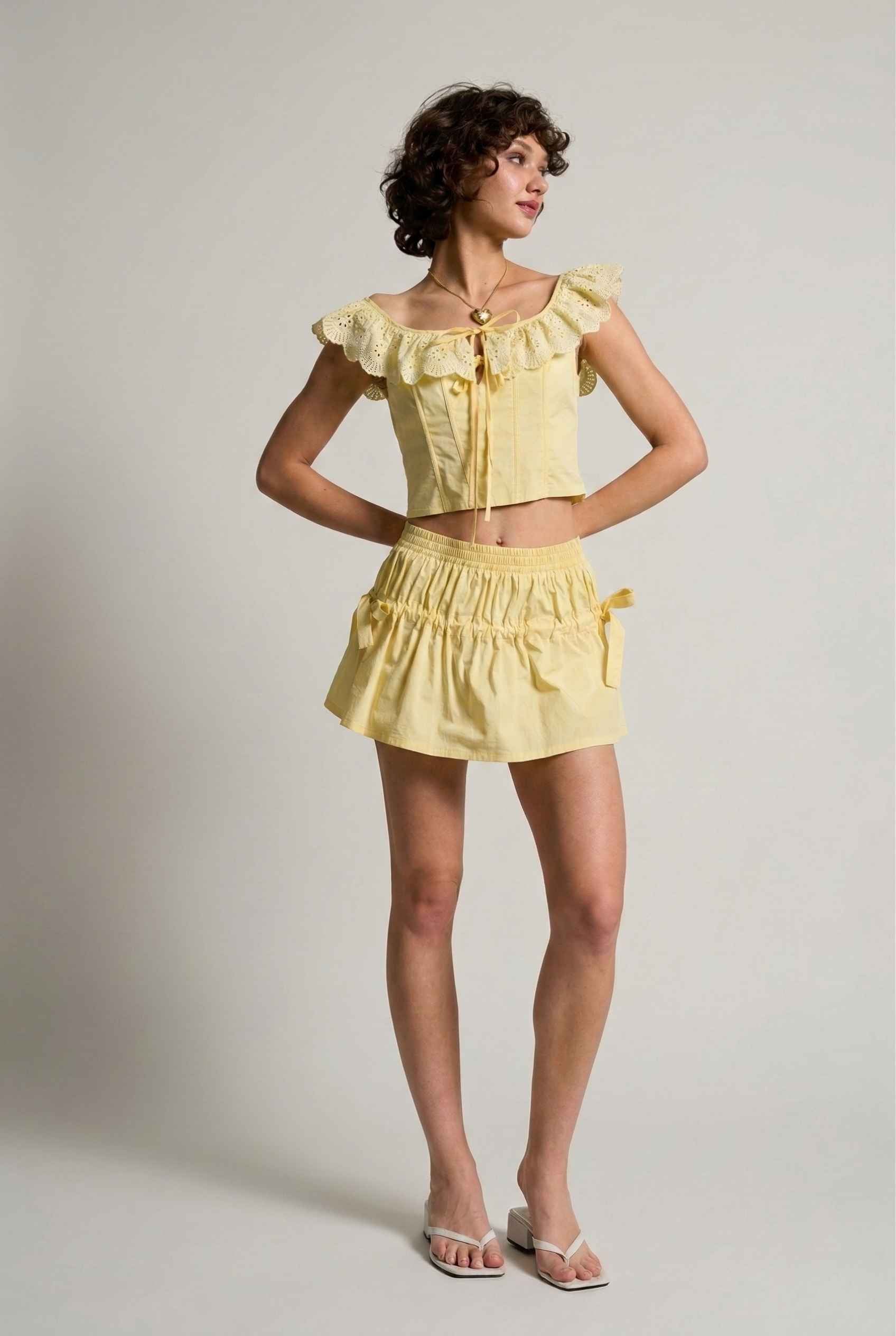 Woman wearing a Clementine Top Lemon Yellow Cotton Eyelet Ruffle Corset plain background