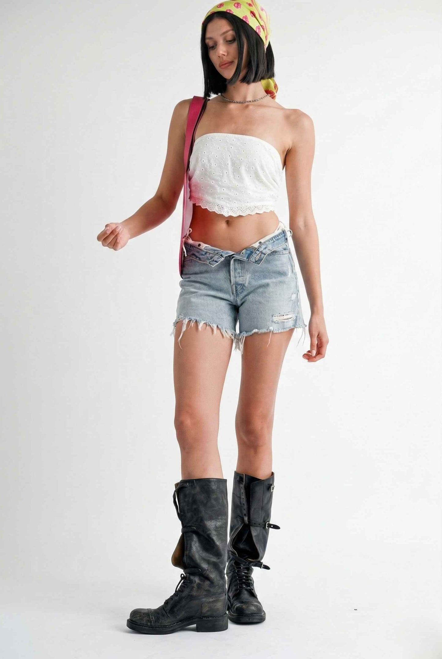 Woman wearing a Clementine Top White Cotton Eyelet Strapless Crop, denim shorts, and black boots on a white background