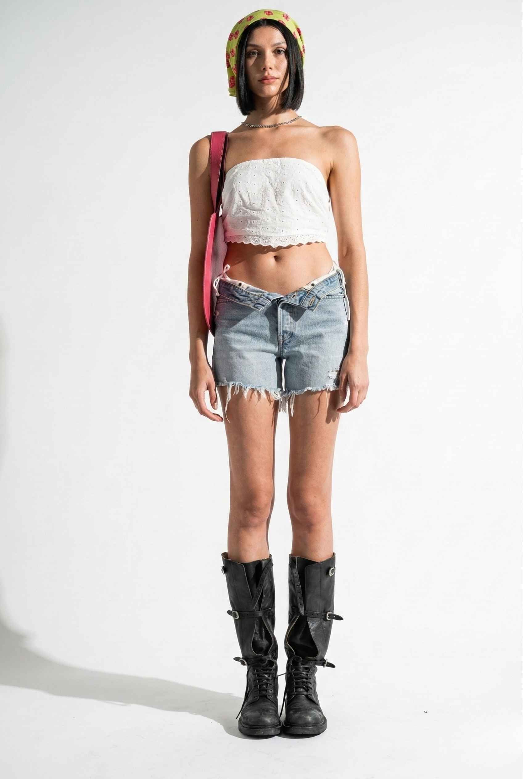 Woman wearing a Clementine Top White Cotton Eyelet Strapless Crop, denim shorts, and black boots on a white background