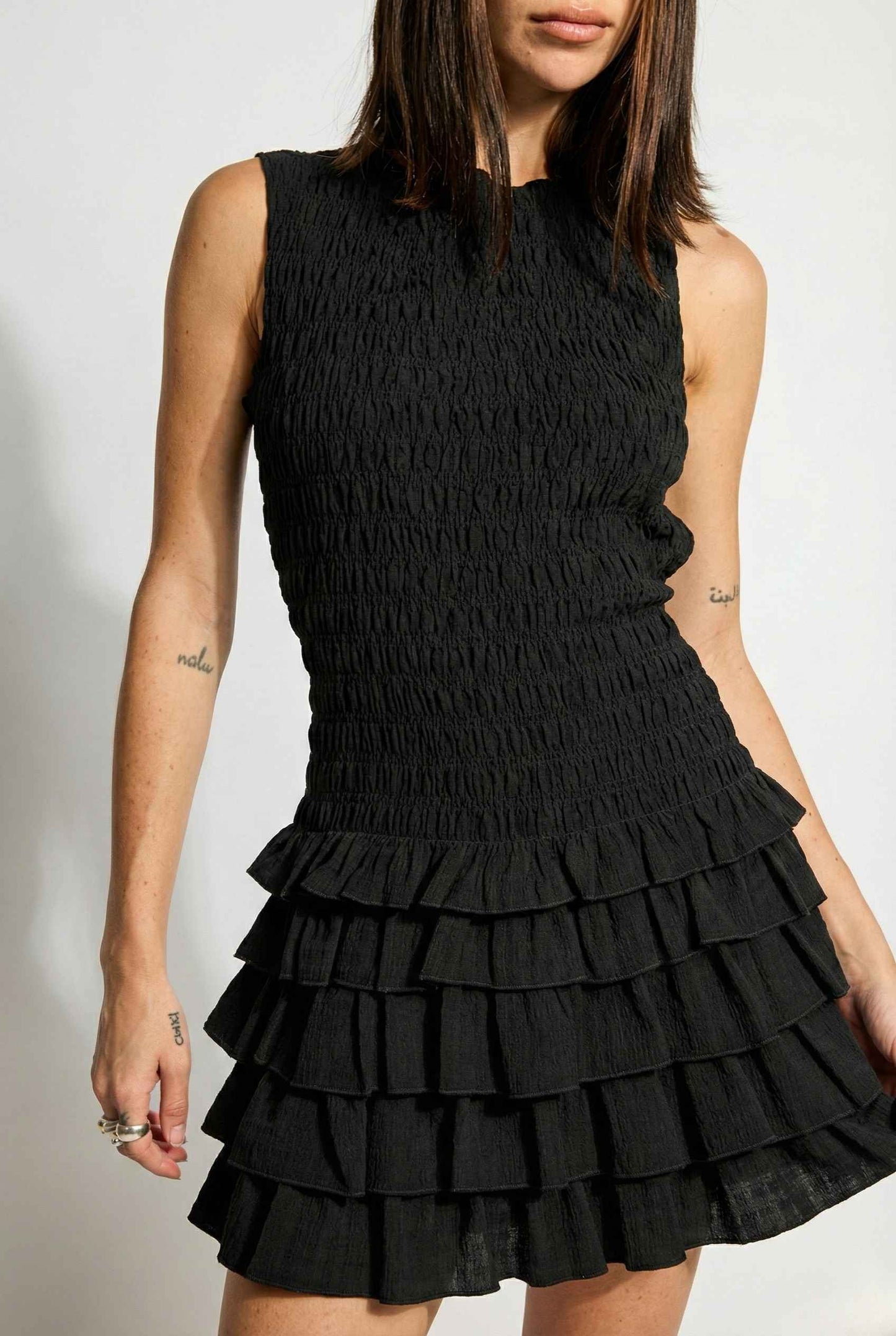 Cleo Mini Black Smocked Ruffle Sleeveless Dress worn by a woman on a plain background