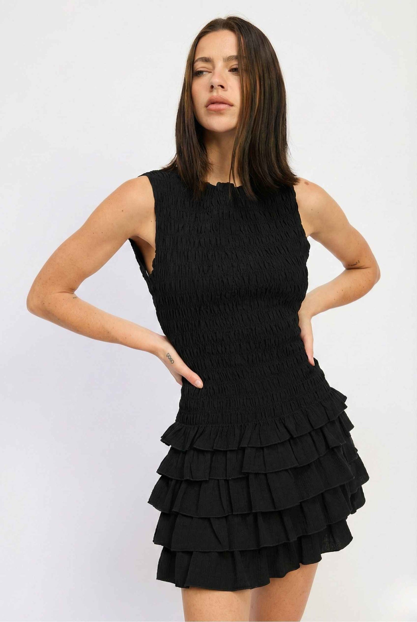 Woman wearing a Cleo Mini Black Smocked Ruffle Sleeveless Dress against a white background
