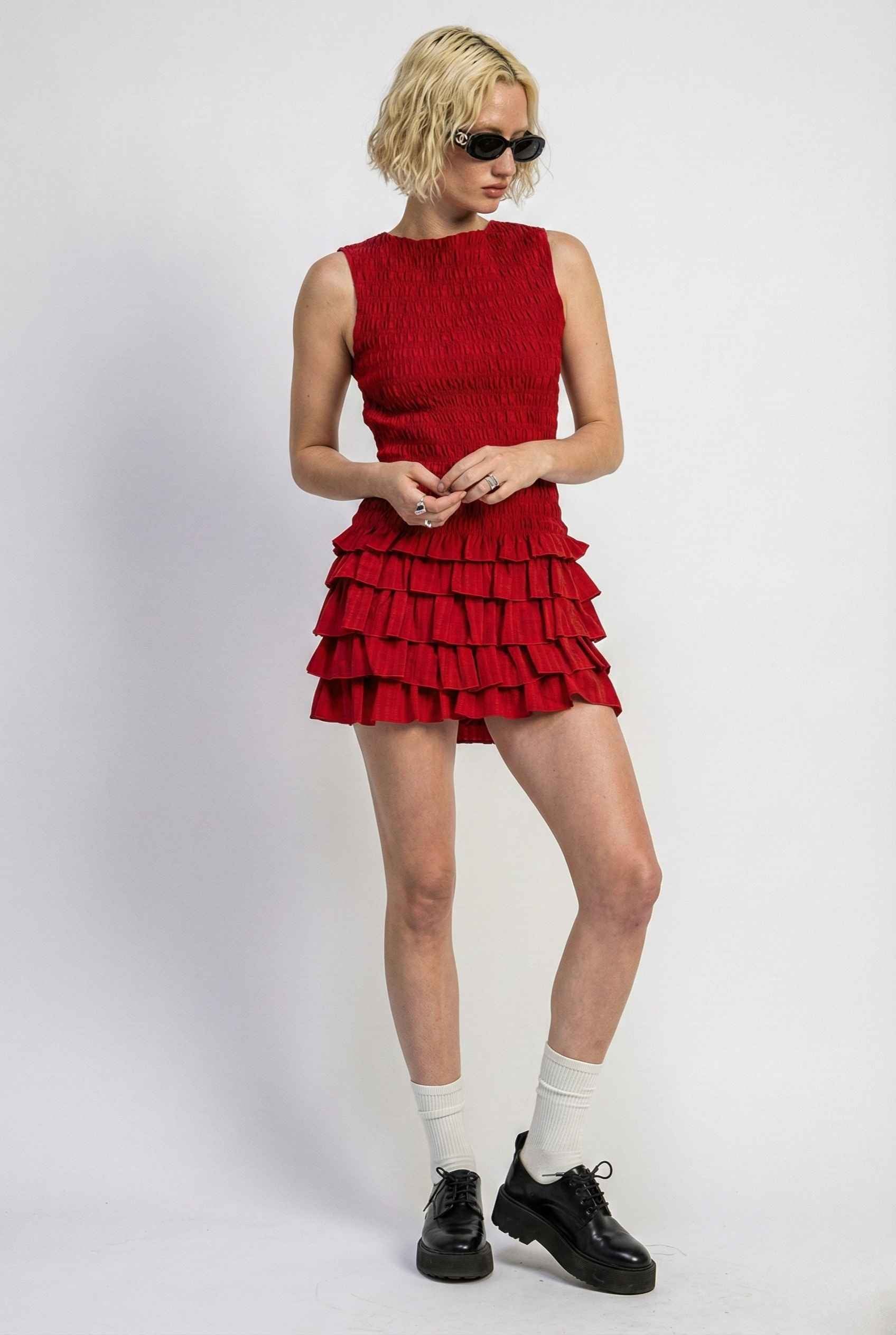 Person wearing a Cleo Mini Red Smocked Ruffle Sleeveless Dress with ruffled layers on a white background