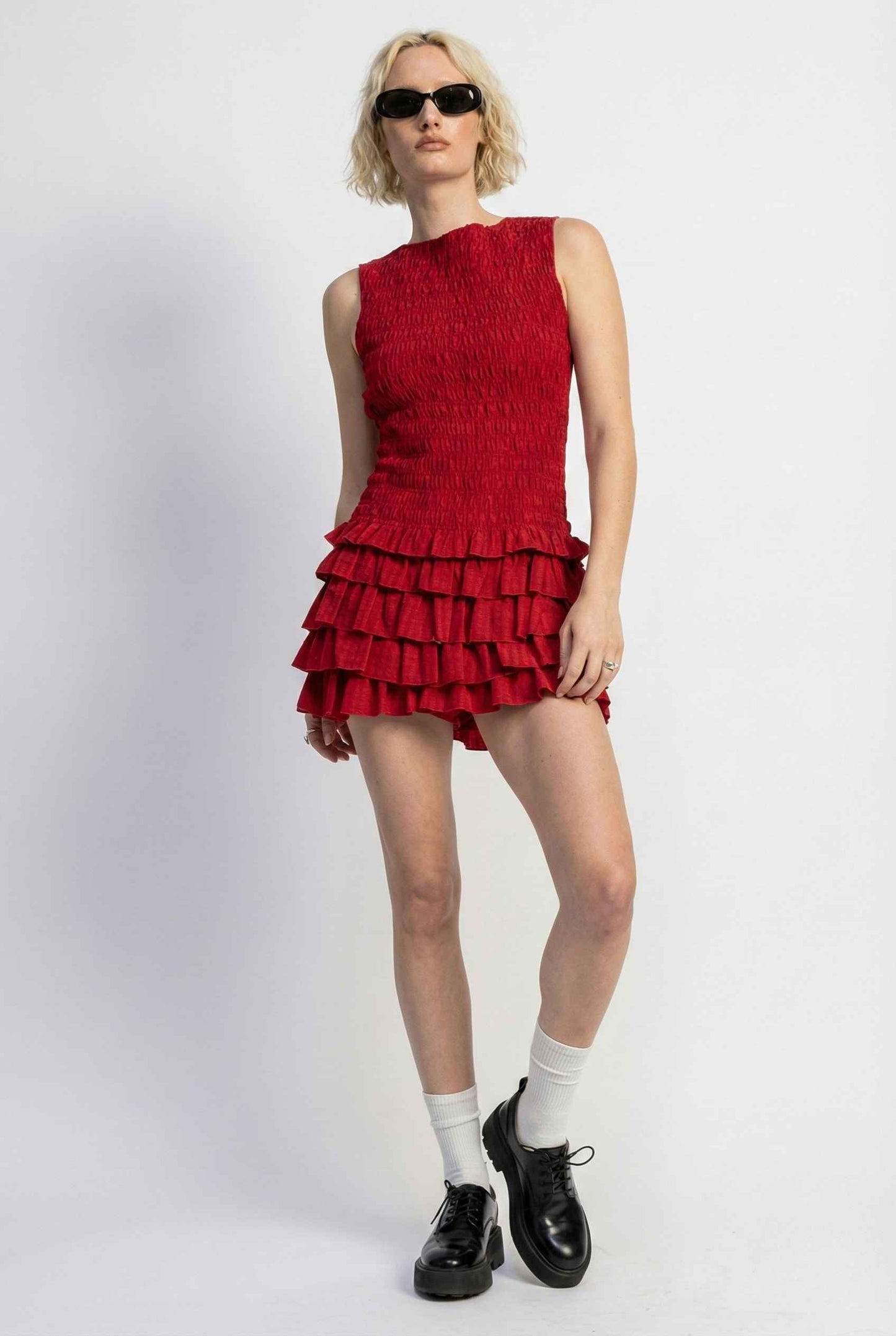 Person wearing a Cleo Mini Red Smocked Ruffle Sleeveless Dress with ruffled layers on a white background