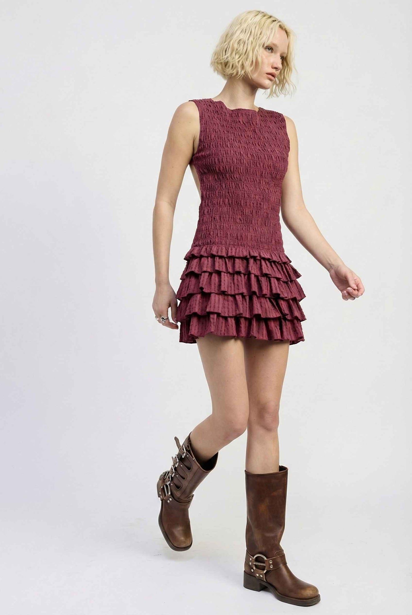 Woman wearing a Cleo Mini Wine Smocked Ruffle Sleeveless Dress with brown boots on a white background