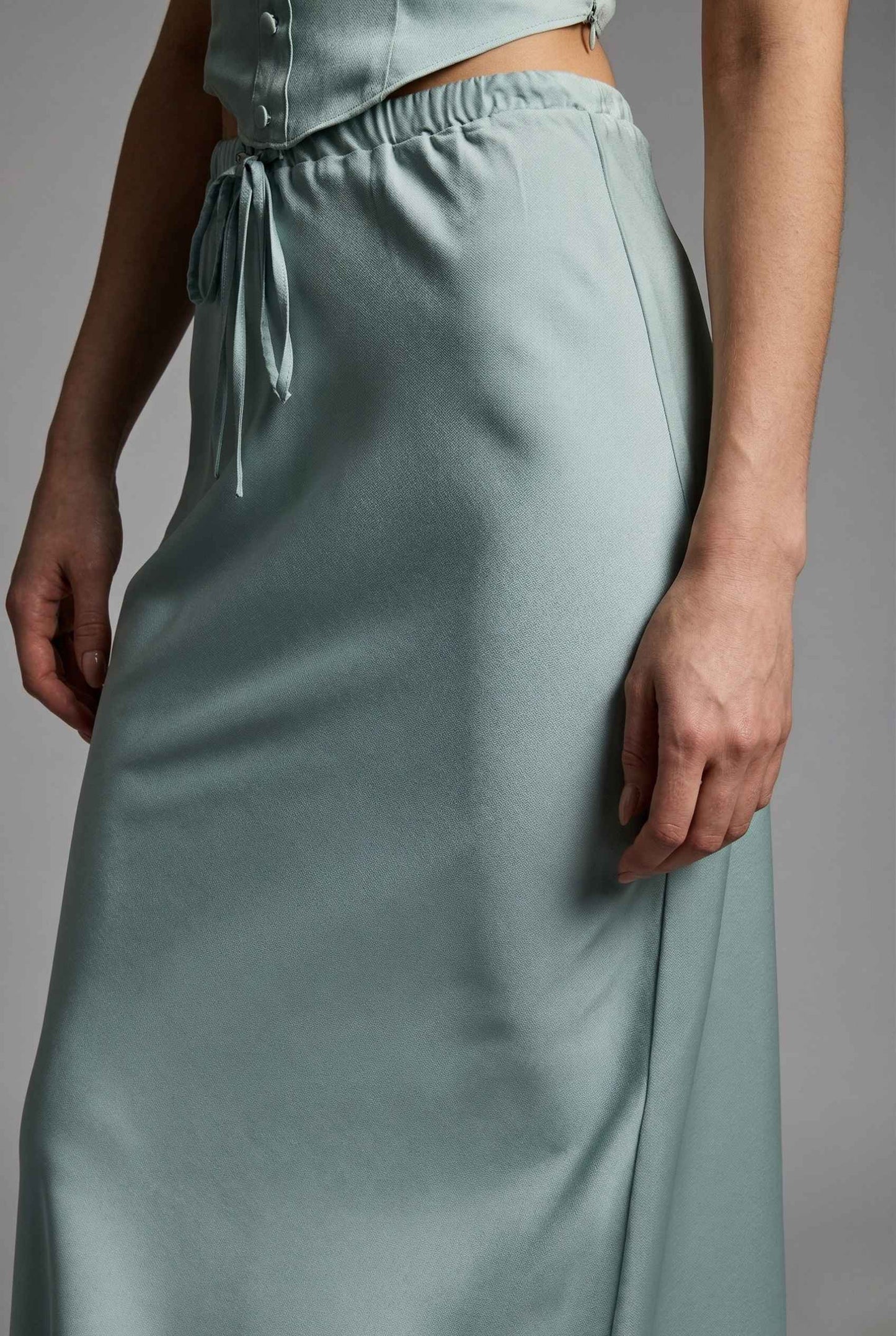 Cleo Skirt Light Blue Satin Drawstring Maxi Skirt worn by a woman on a gray background