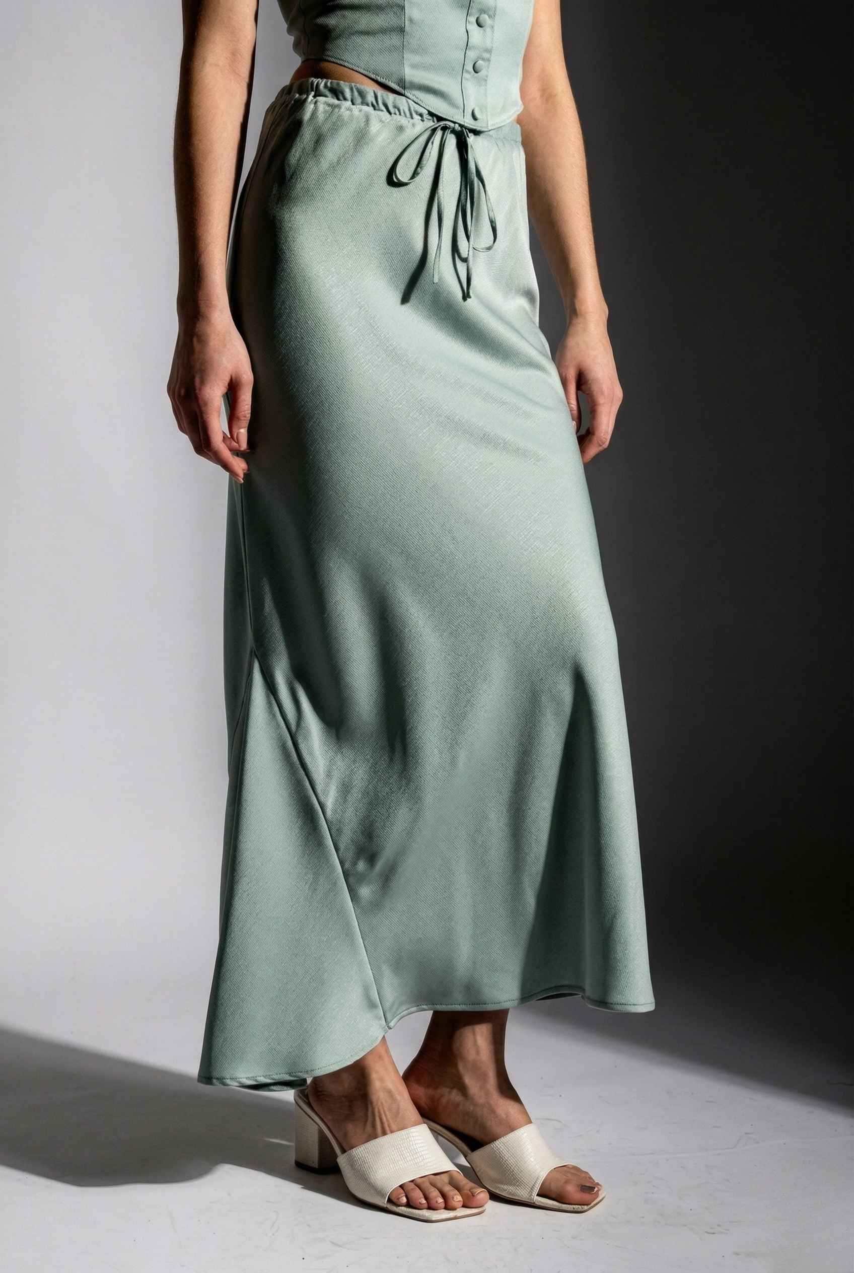 Woman wearing a Cleo Skirt Light Blue Satin Drawstring Maxi Skirt against a gradient background