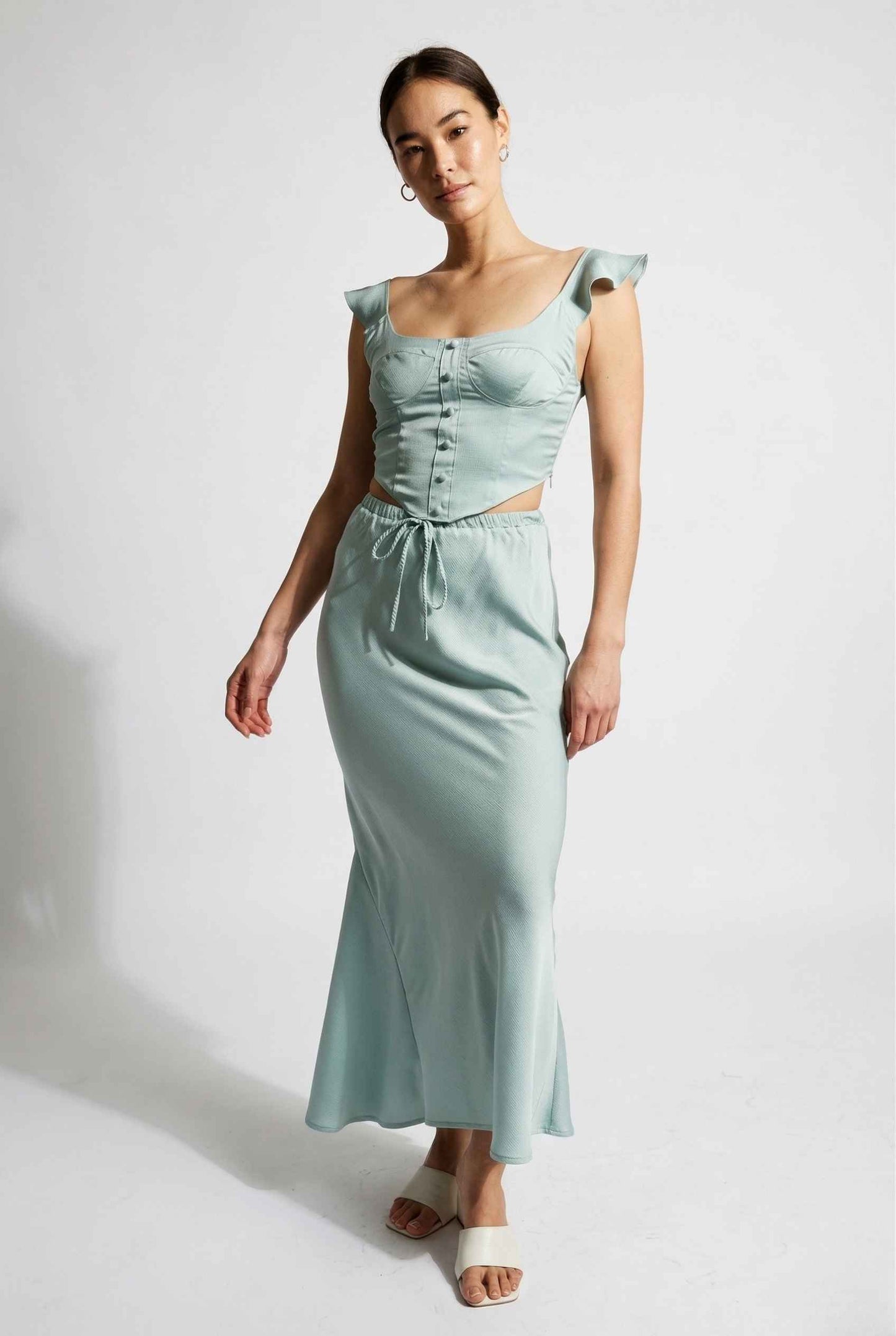 Woman wearing a Cleo Skirt Light Blue Satin Drawstring Maxi Skirt with ruffled sleeves on a white background