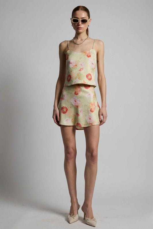 Woman wearing a floral top and Cleo Skirt Light Green Floral Bias-Cut Satin Mini Skirt with sunglasses on a plain background
