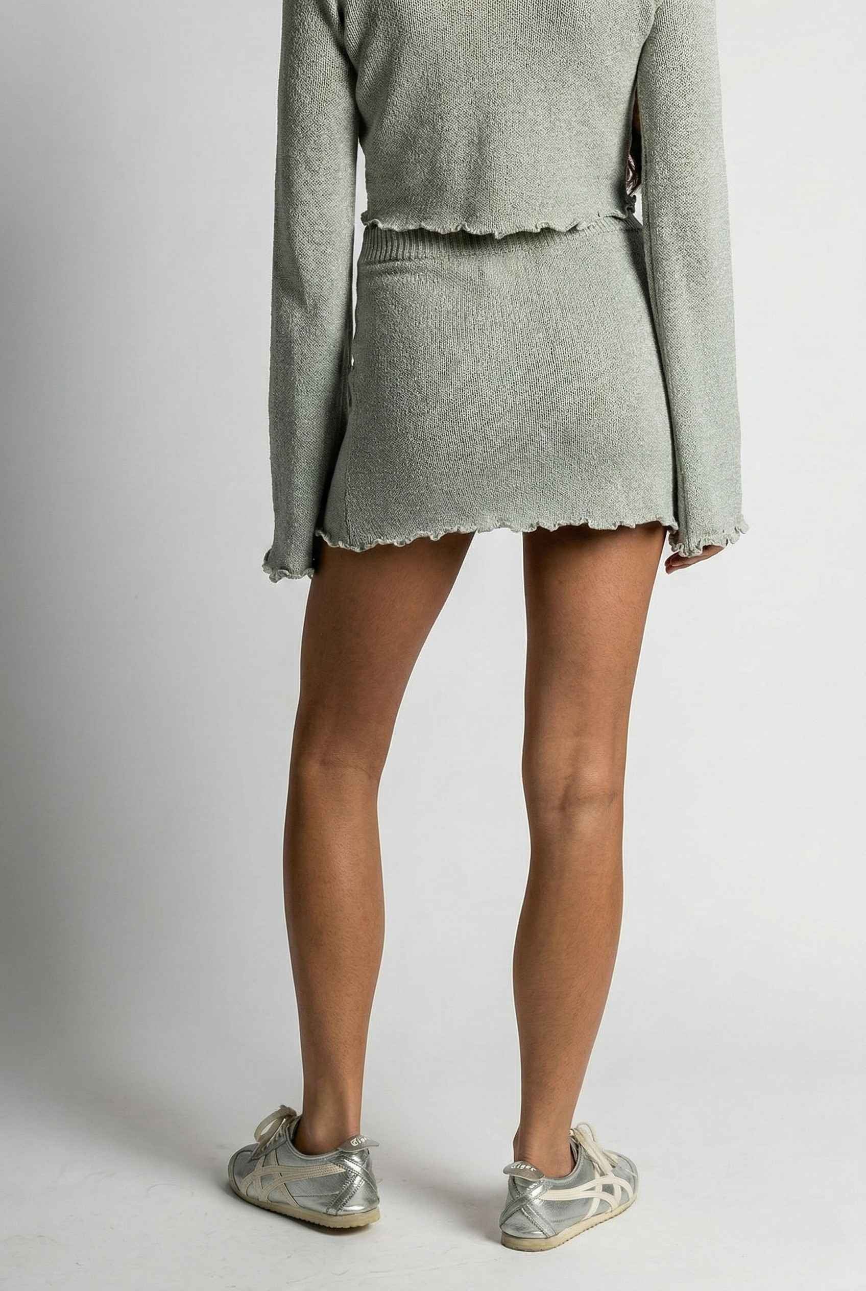 Model wearing Cleo Skirt in Silver Soft Knit Mini Skirt with Drawstring Waist with matching cropped bolero and sneakers on a plain background