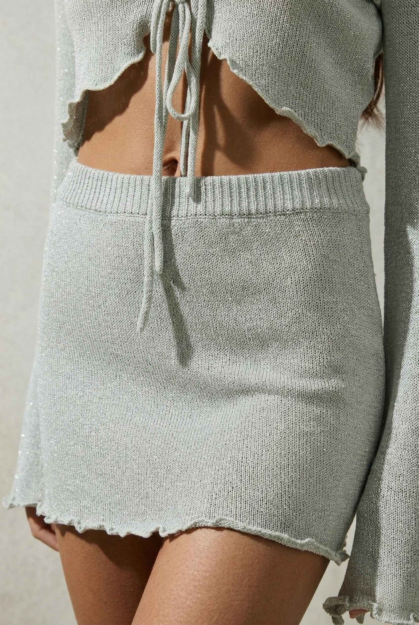 Model wearing Cleo Skirt in Silver Soft Knit Mini Skirt with Drawstring Waist with matching cropped bolero on a plain background