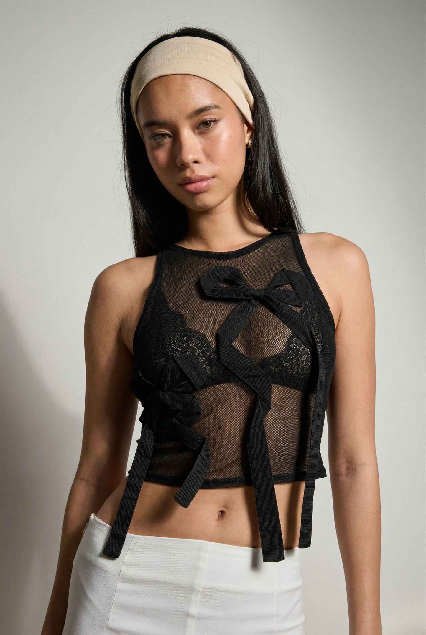 Woman wearing a Colette Top Black Sheer Mesh Ribbon Bow Tank with bows and pants against a plain background