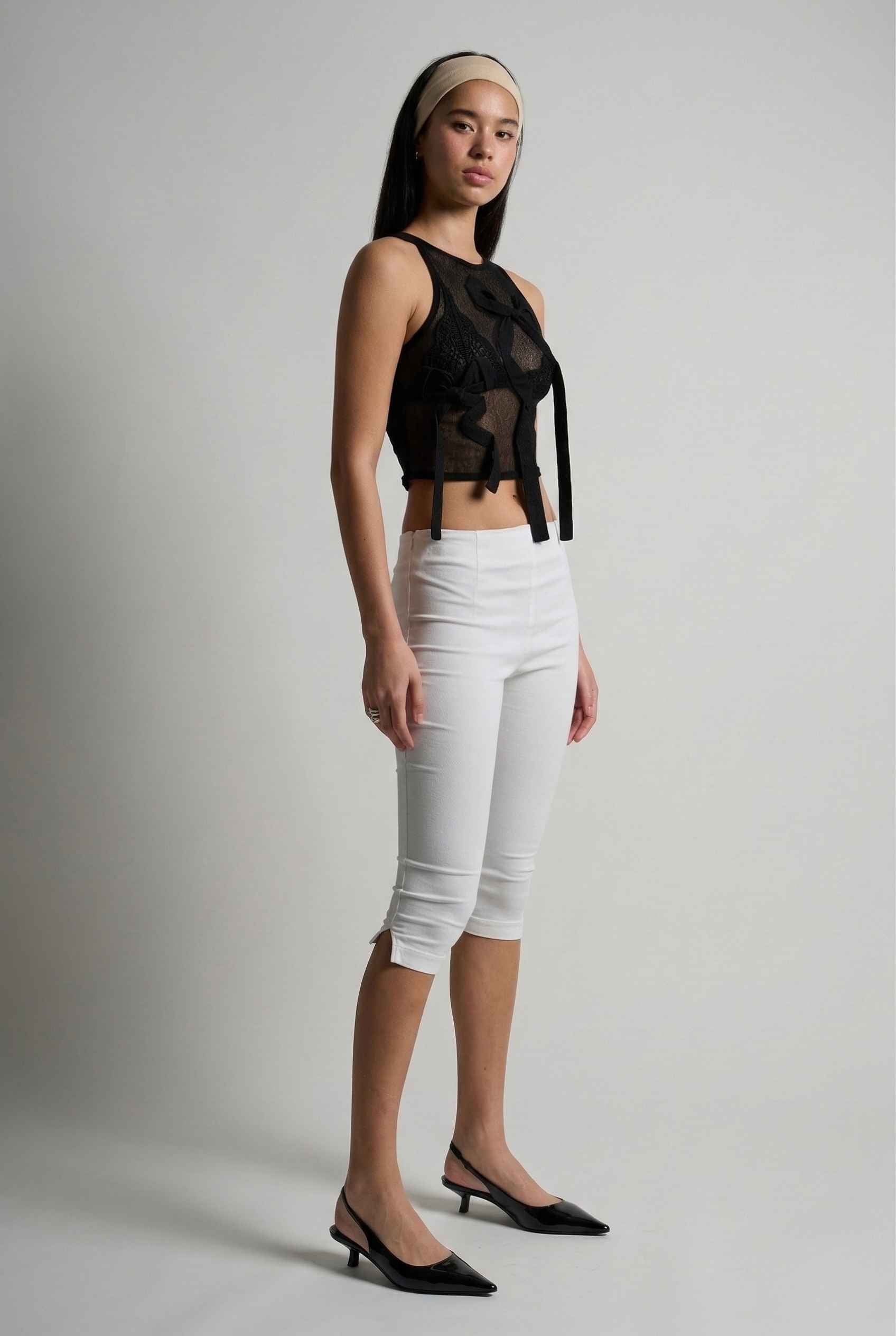 Woman wearing a Colette Top Black Sheer Mesh Ribbon Bow Tank and  pants against a plain background