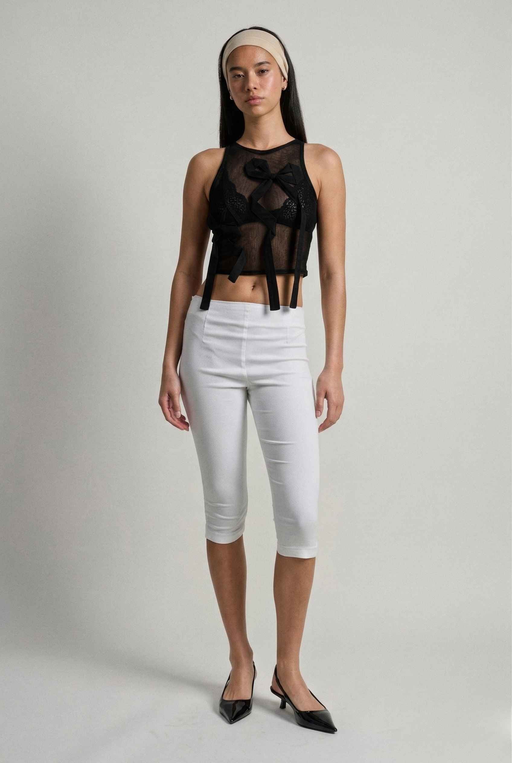 Woman wearing a Colette Top Black Sheer Mesh Ribbon Bow Tank and  pants on a plain background
