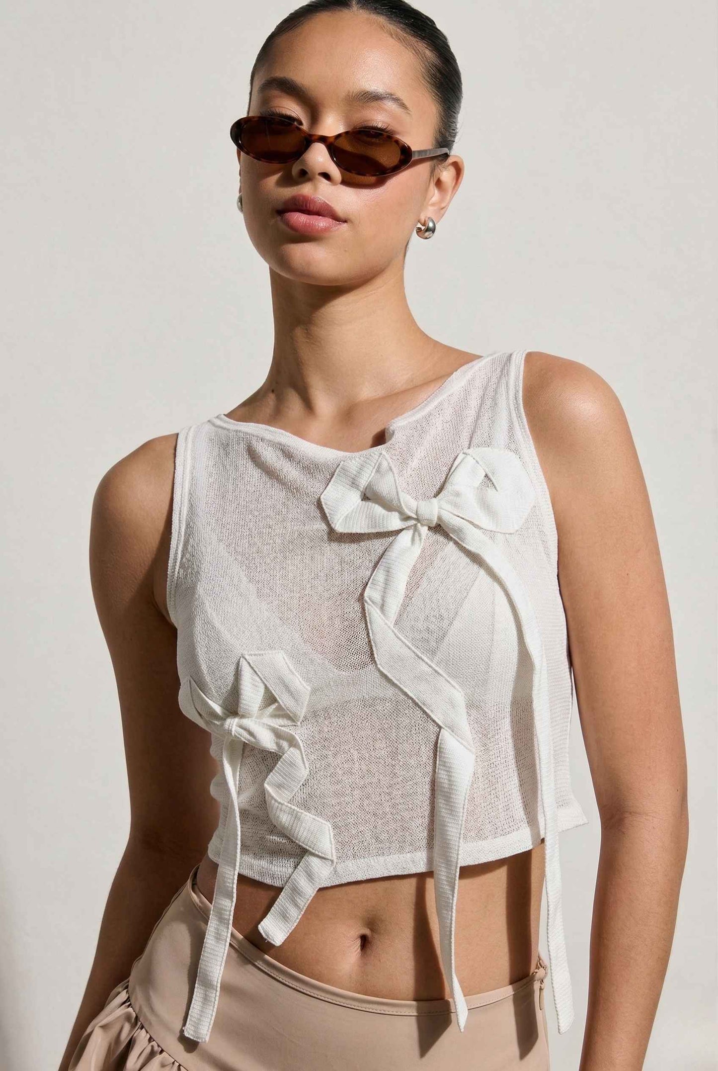 Woman wearing a Colette Top White Sheer Mesh Ribbon Bow Tank with white ruffles and sunglasses on a plain background