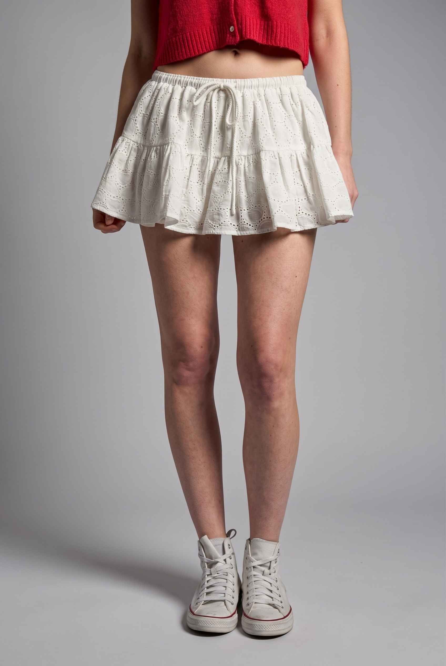 Model wearing Corinne Cotton Skort Pleated Ruffle Mini Skort in White with cropped short sleeve cardigan and sneakers
