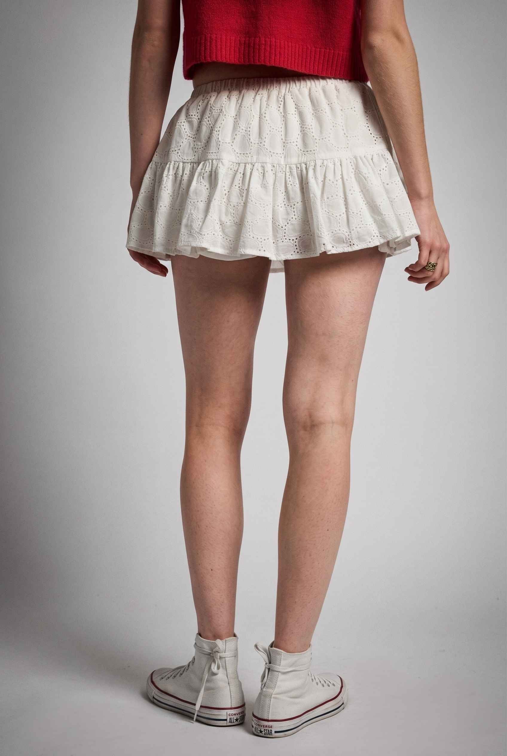 Model wearing Corinne  Cotton Skort Pleated Ruffle Mini Skort in White with cropped short sleeve cardigan and sneakers