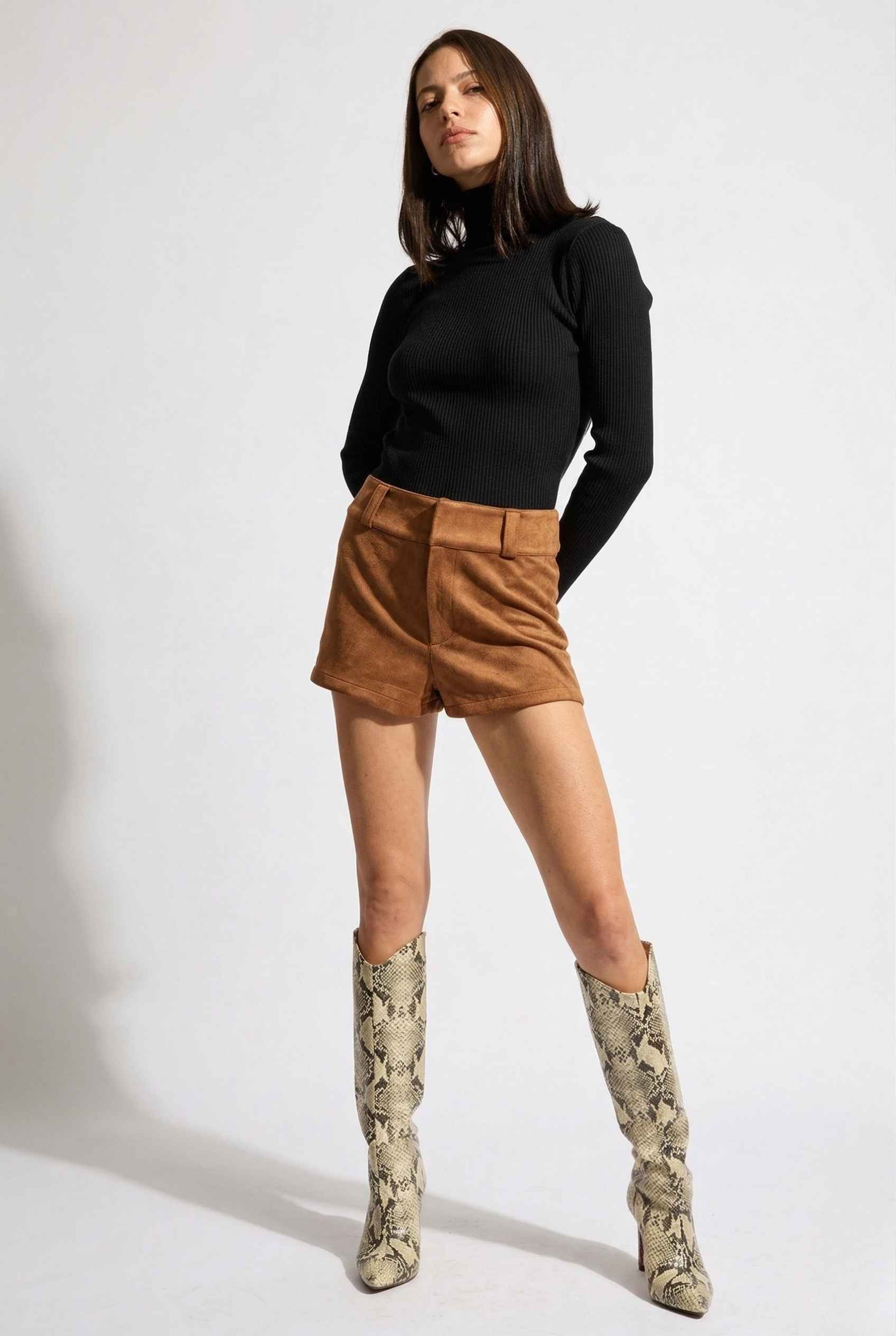 Woman wearing a black turtleneck, Dakota Shorts Brown Faux Suede Low-Rise Mini Shorts, and patterned boots on a white background