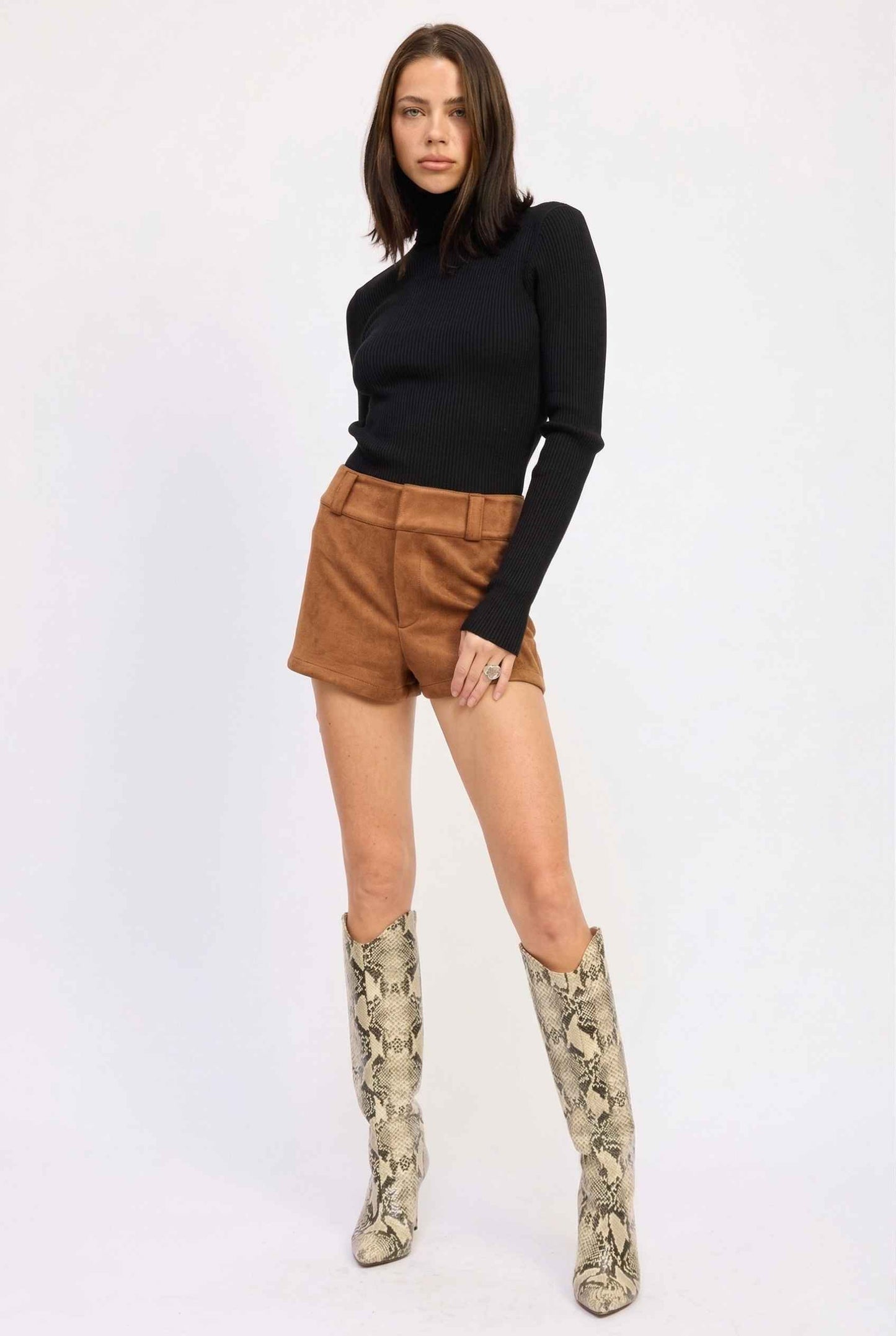 Woman wearing a black turtleneck, Dakota Shorts Brown Faux Suede Low-Rise Mini Shorts, and patterned knee-high boots on a white background