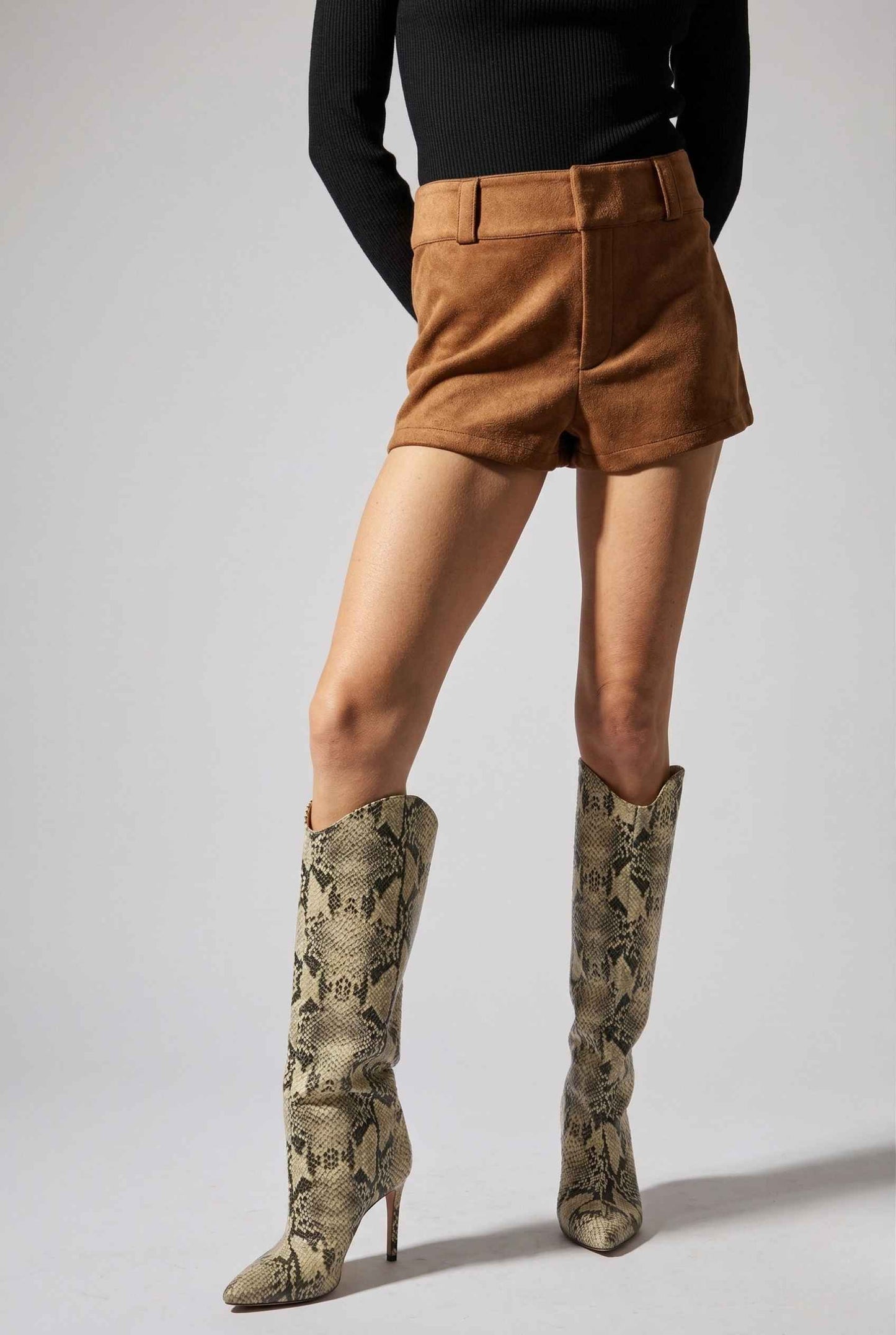 Woman wearing Dakota Shorts Brown Faux Suede Low-Rise Mini Shorts and snake print knee-high boots on a white background