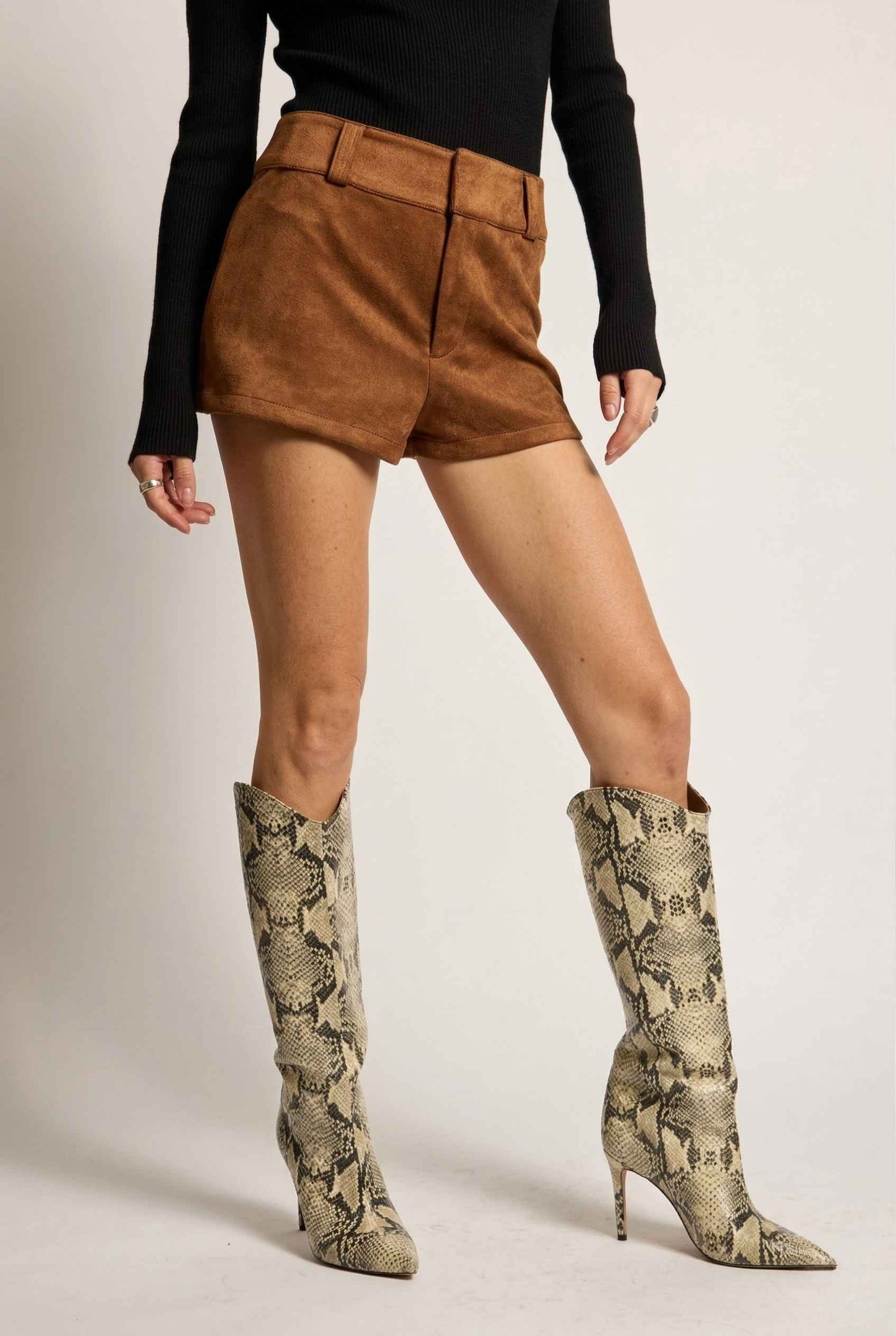 Woman wearing Dakota Shorts Brown Faux Suede Low-Rise Mini Shorts and snake print knee-high boots on a plain background