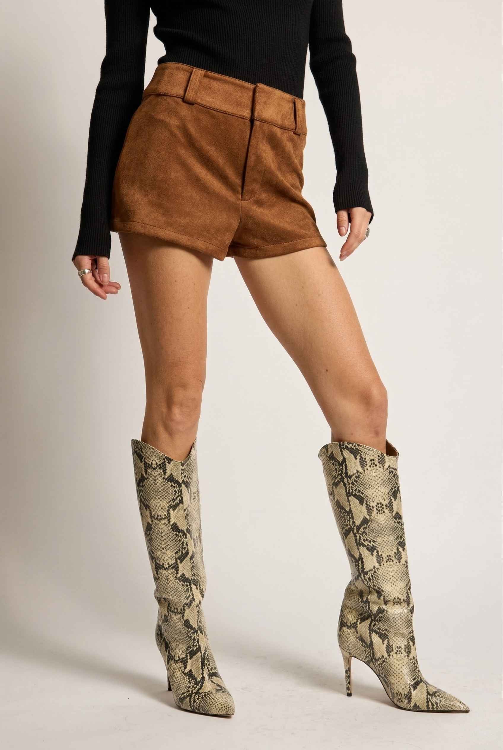 Woman wearing Dakota Shorts Brown Faux Suede Low-Rise Mini Shorts and snake print knee-high boots on a plain background