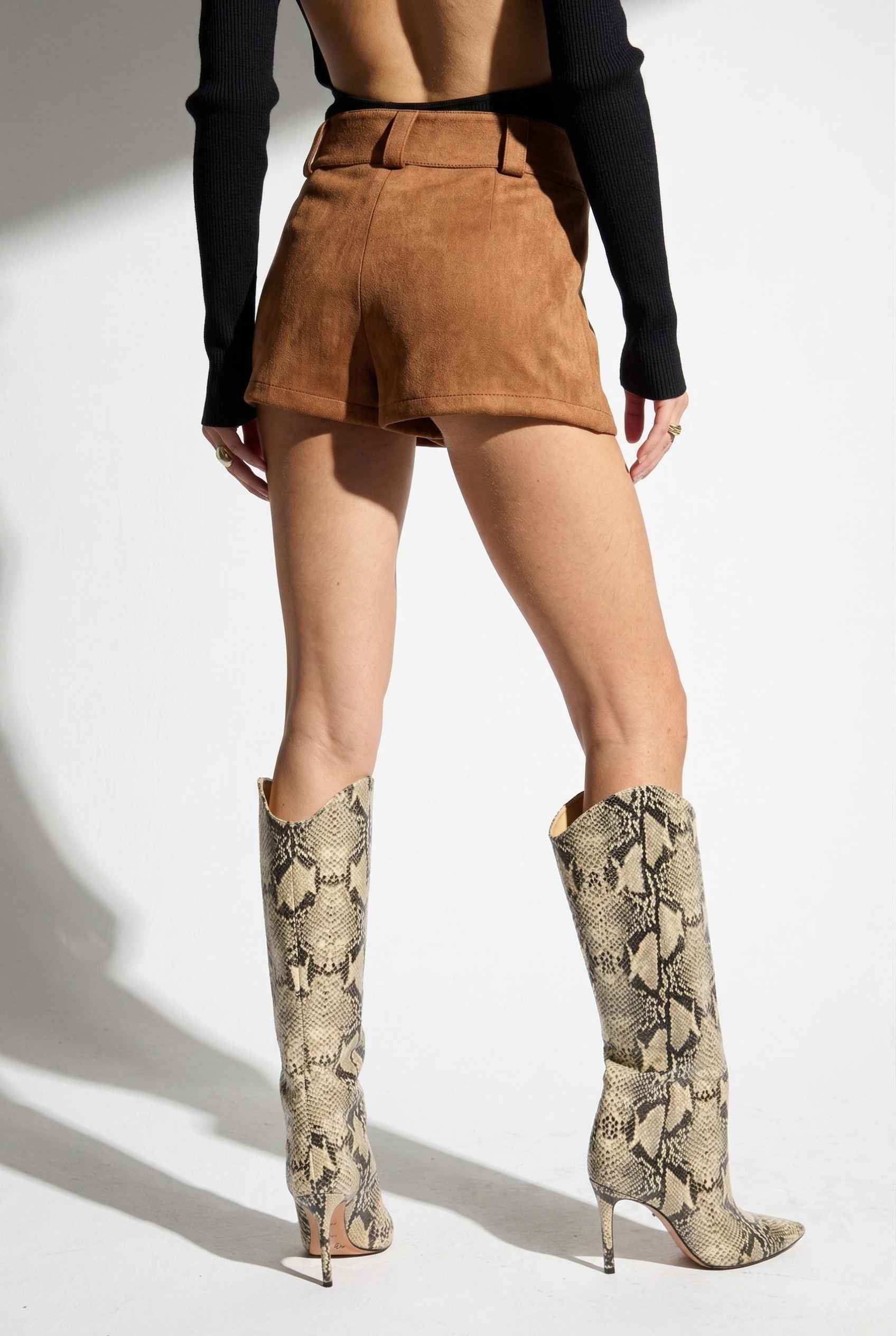 Woman wearing Dakota Shorts Brown Faux Suede Low-Rise Mini Shorts and snake print knee-high boots on a white background